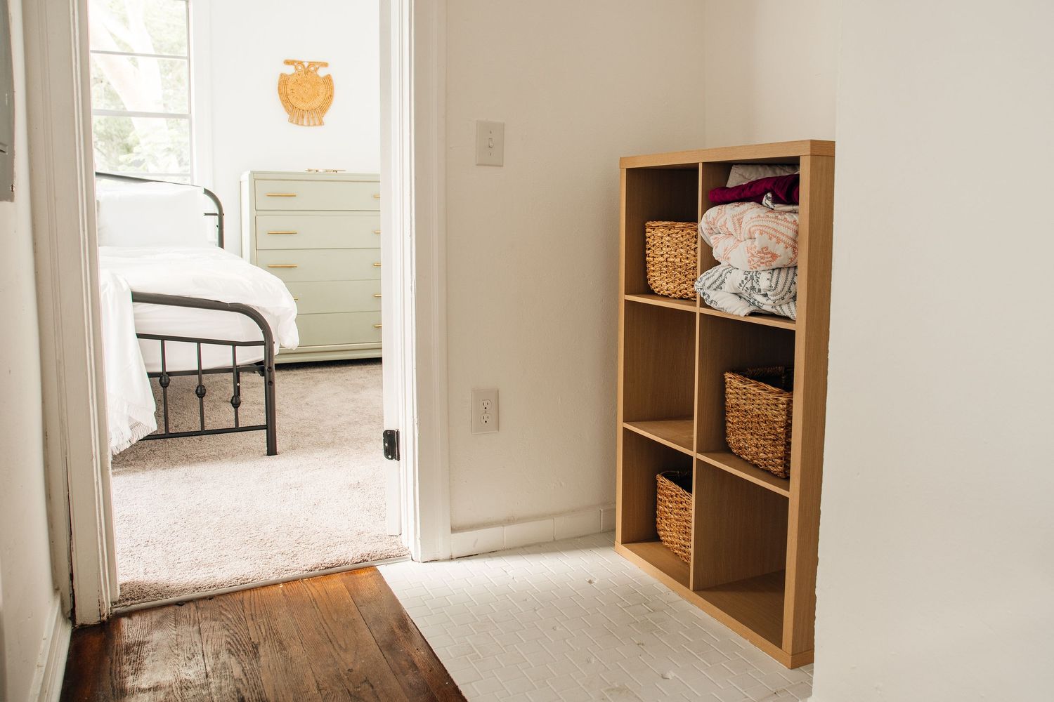 Small wooden cubby shelf with wicker baskets near a bright bedroom doorway.