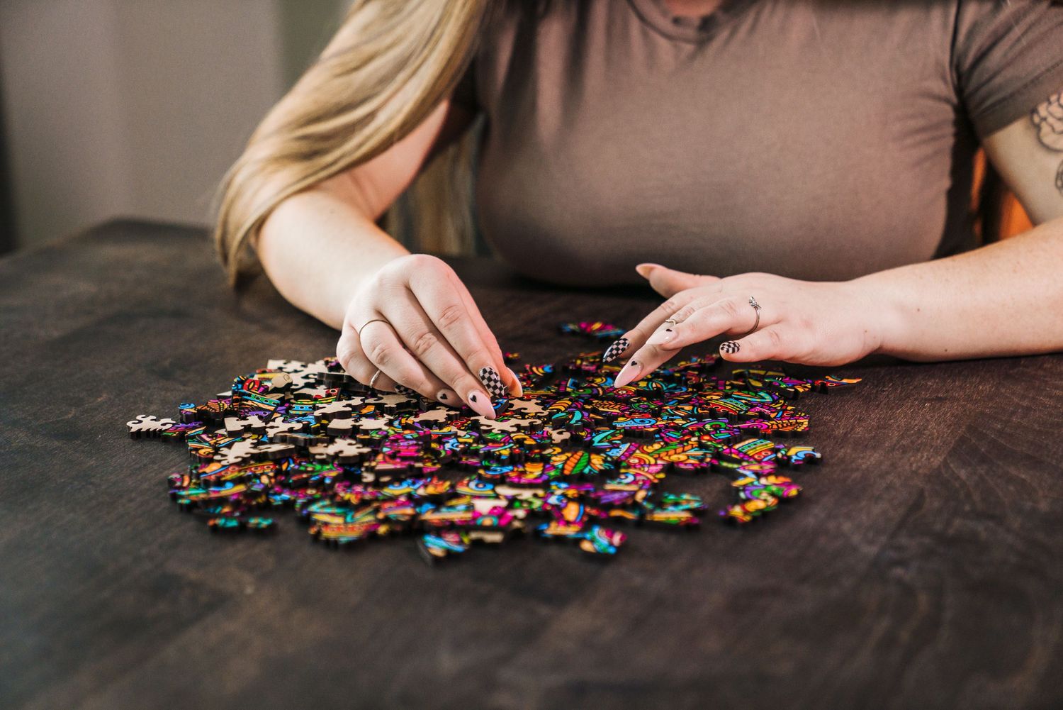 Woman sorting colorful jigsaw puzzle pieces on a dark wooden table, working on assembling a vibrant puzzle.