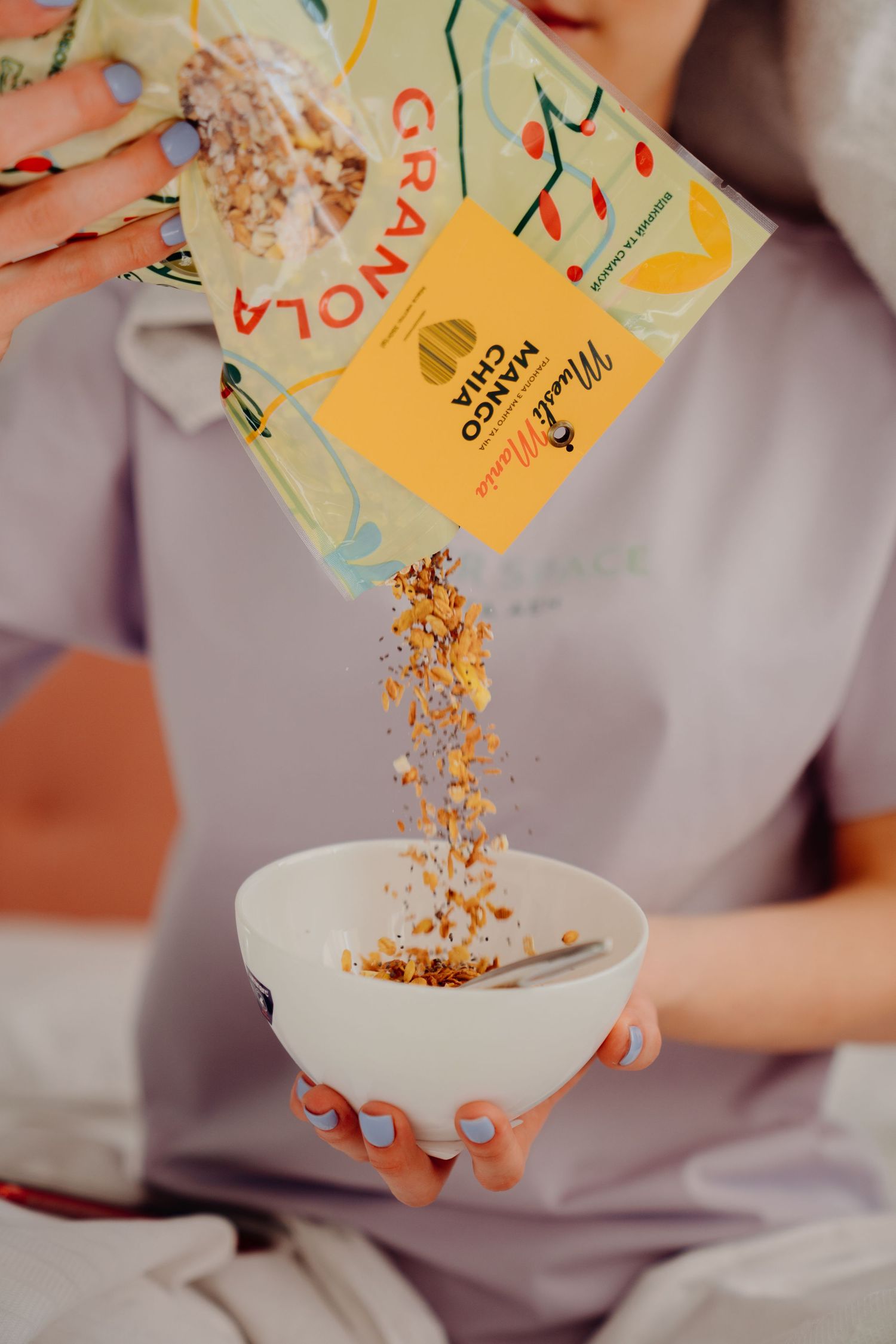 Woman pouring MuesliMania Mango China granola from yellow package into white ceramic bowl.
