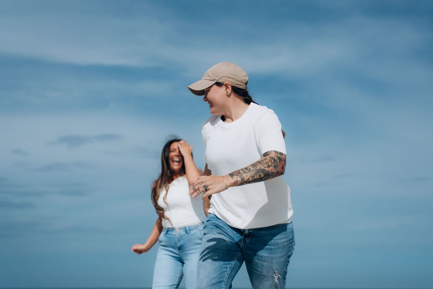 Couple in casual beach attire sharing joyful moments against blue sky.
