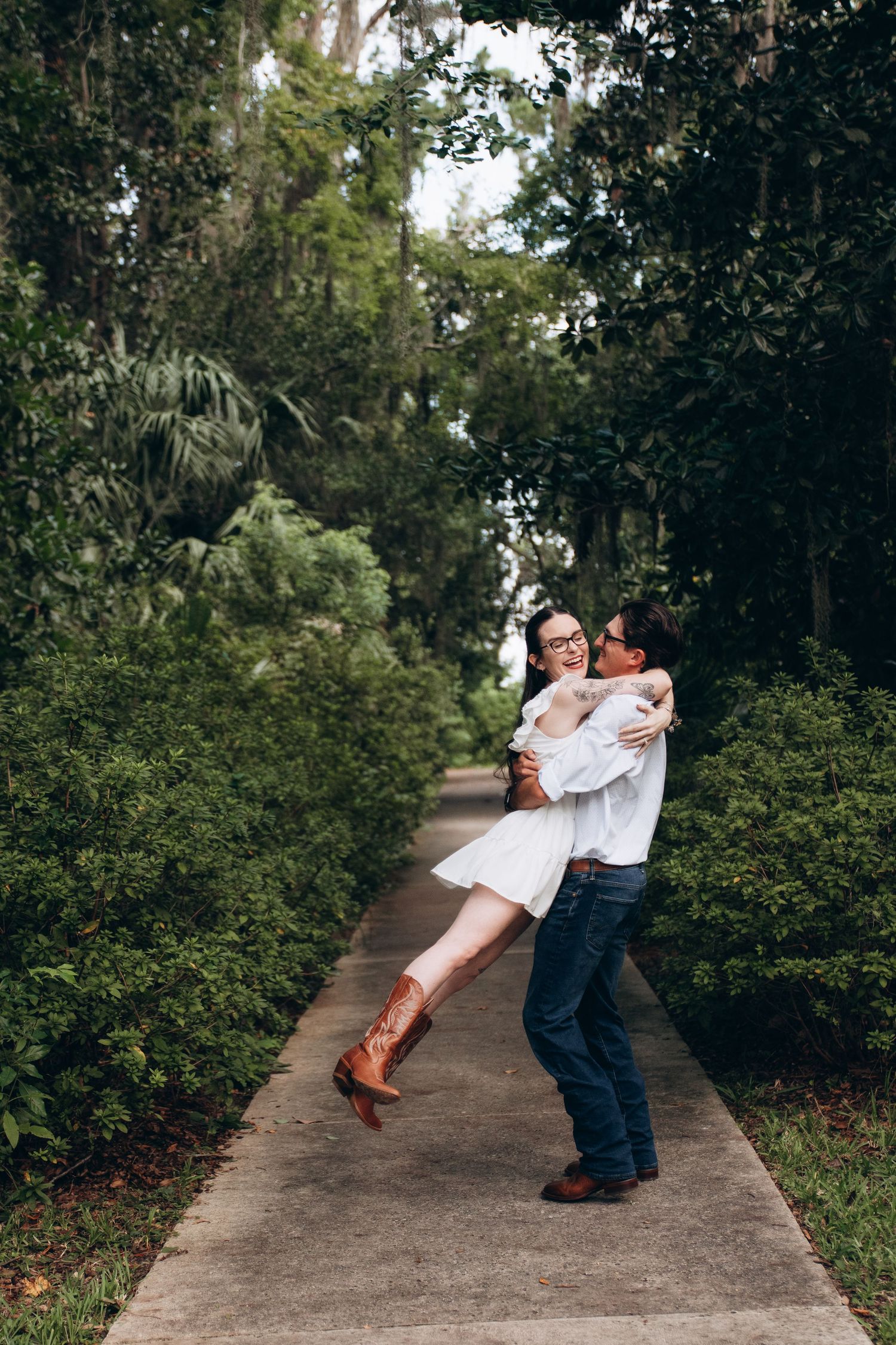 A playful moment captured on a garden path with brown cowboy boots and white summer attire.