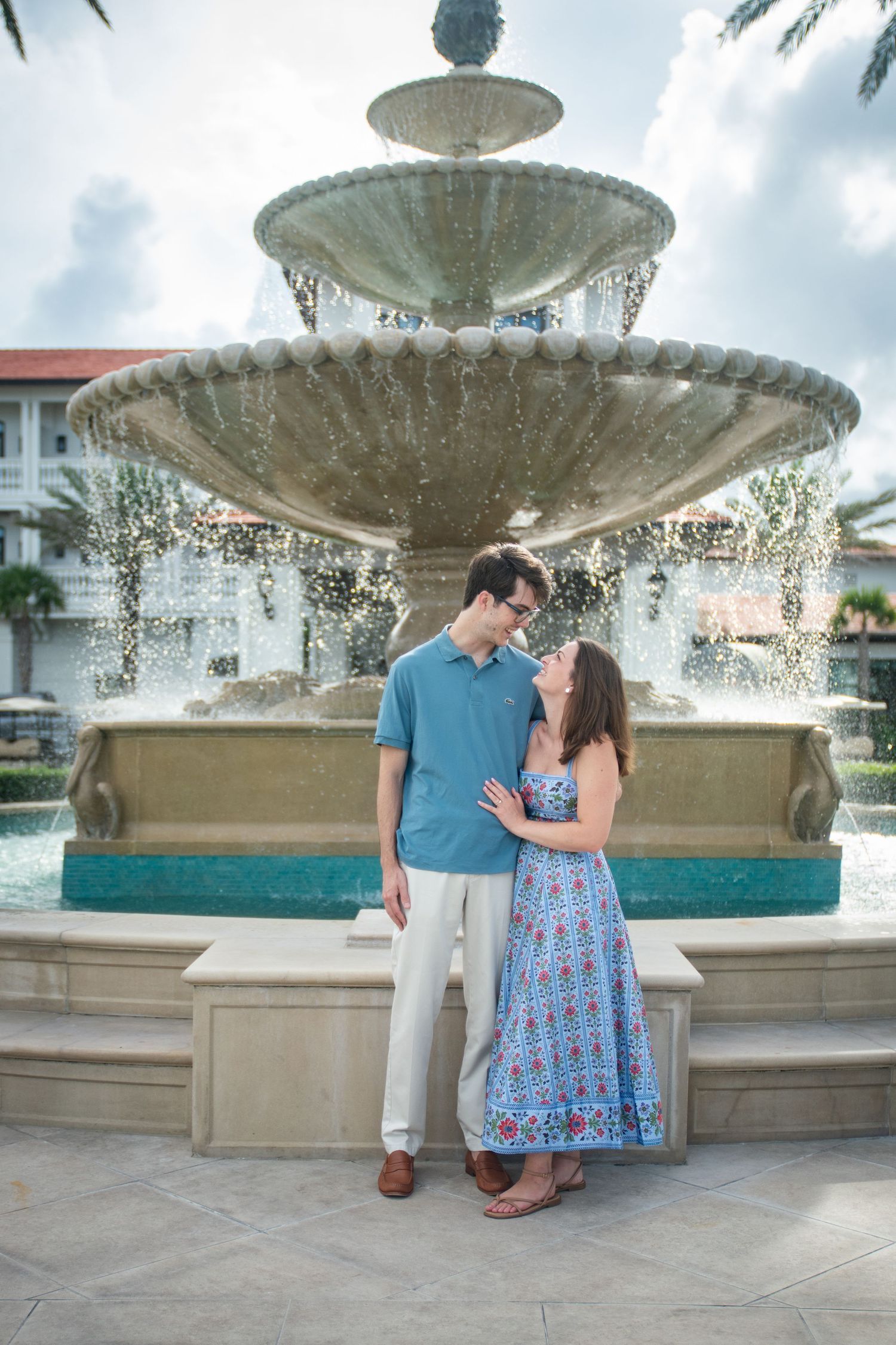 A couple shares romantic moments by a decorative fountain with spraying water in an outdoor plaza.