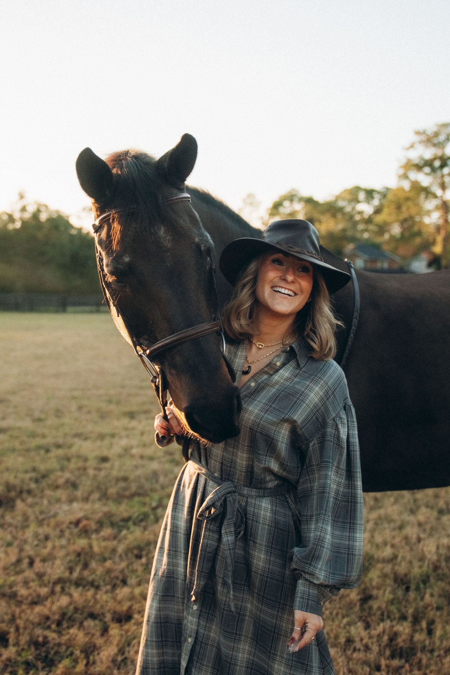 A joyful moment shared between a dark horse and companion wearing plaid and a wide-brimmed hat.