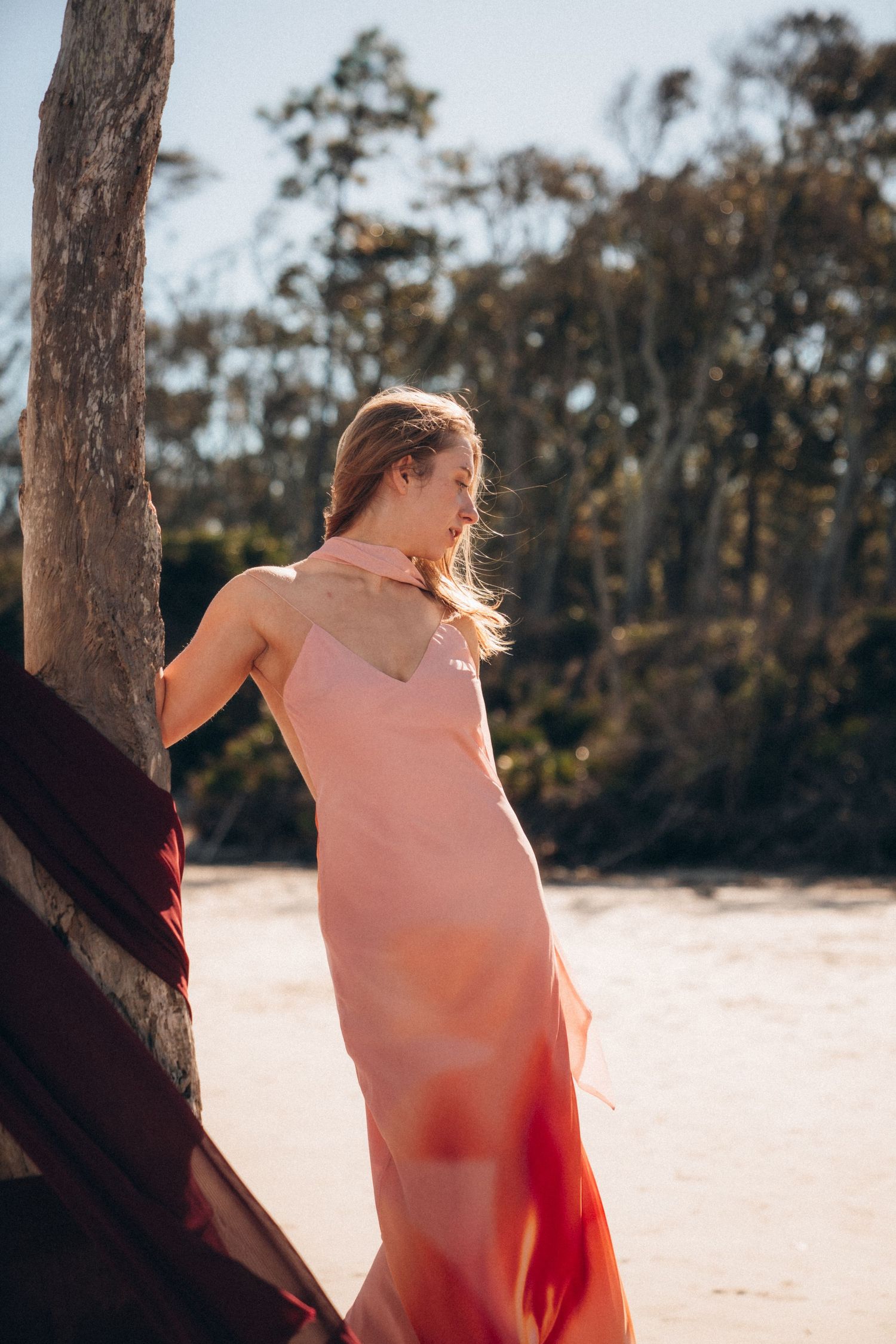 Dreamy beach scene with figure in flowing fabric against trees and sand.