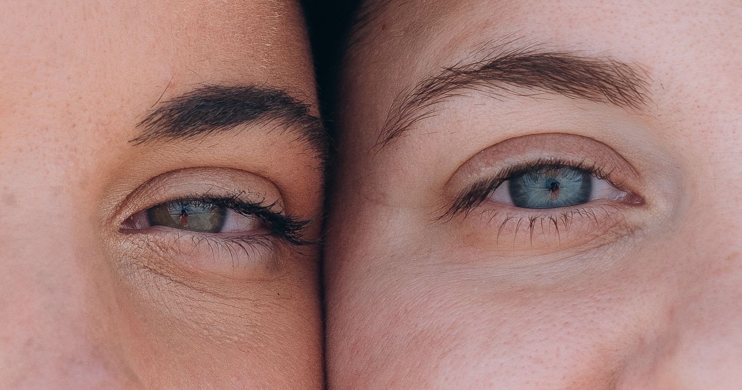 Extreme close-up of bright blue eyes and natural eyebrows against a pink background.