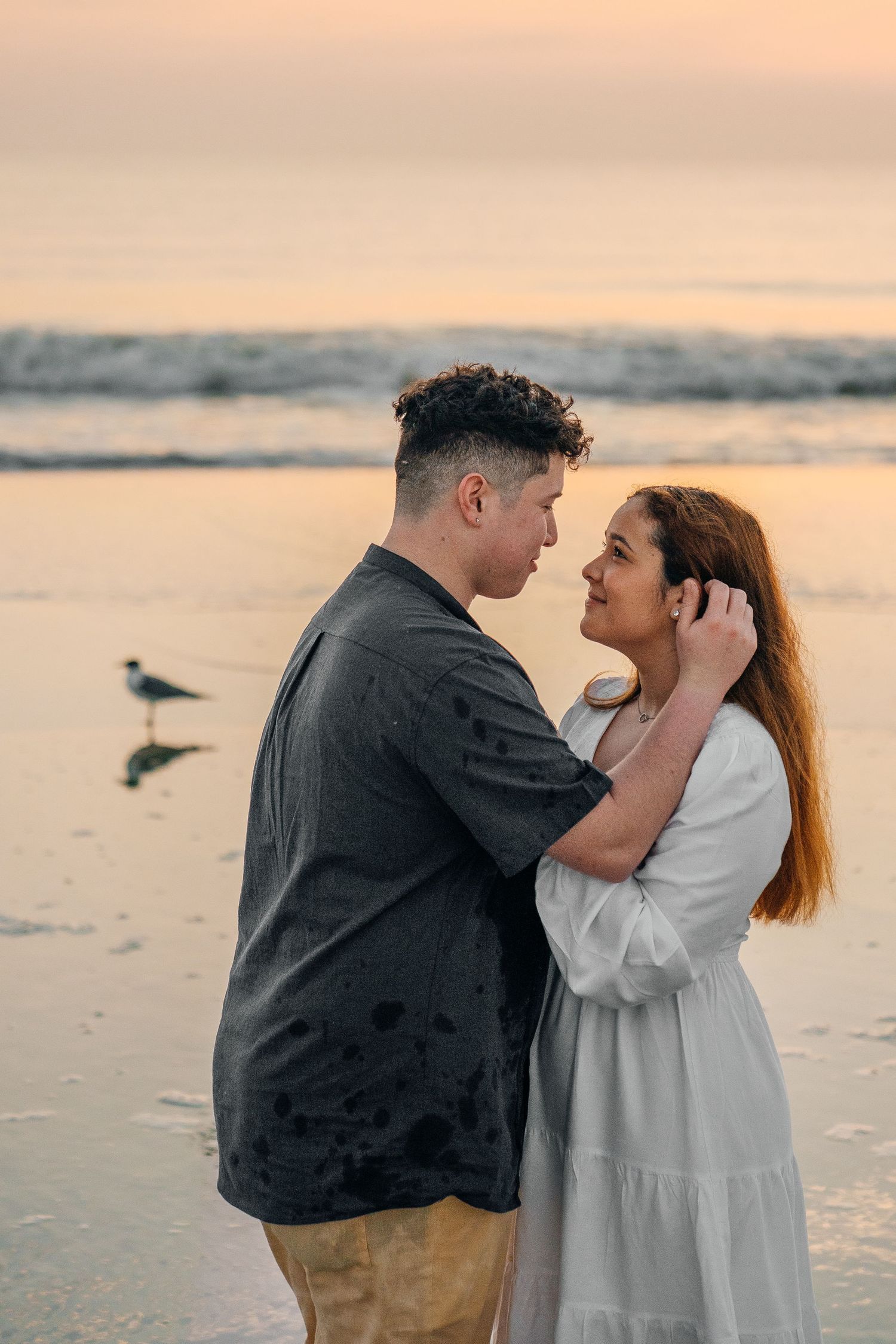 A couple dressed in white and black sharing a romantic moment on a sandy beach.