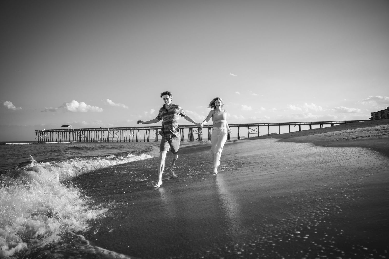 Wide angle black and white beach photos showing a couple running along the shoreline.