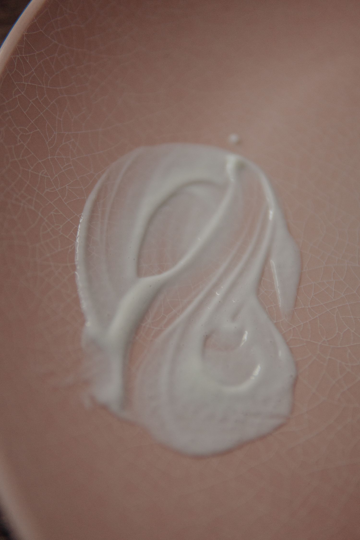 White moisturizing cream swirl texture smeared on a pink ceramic plate.