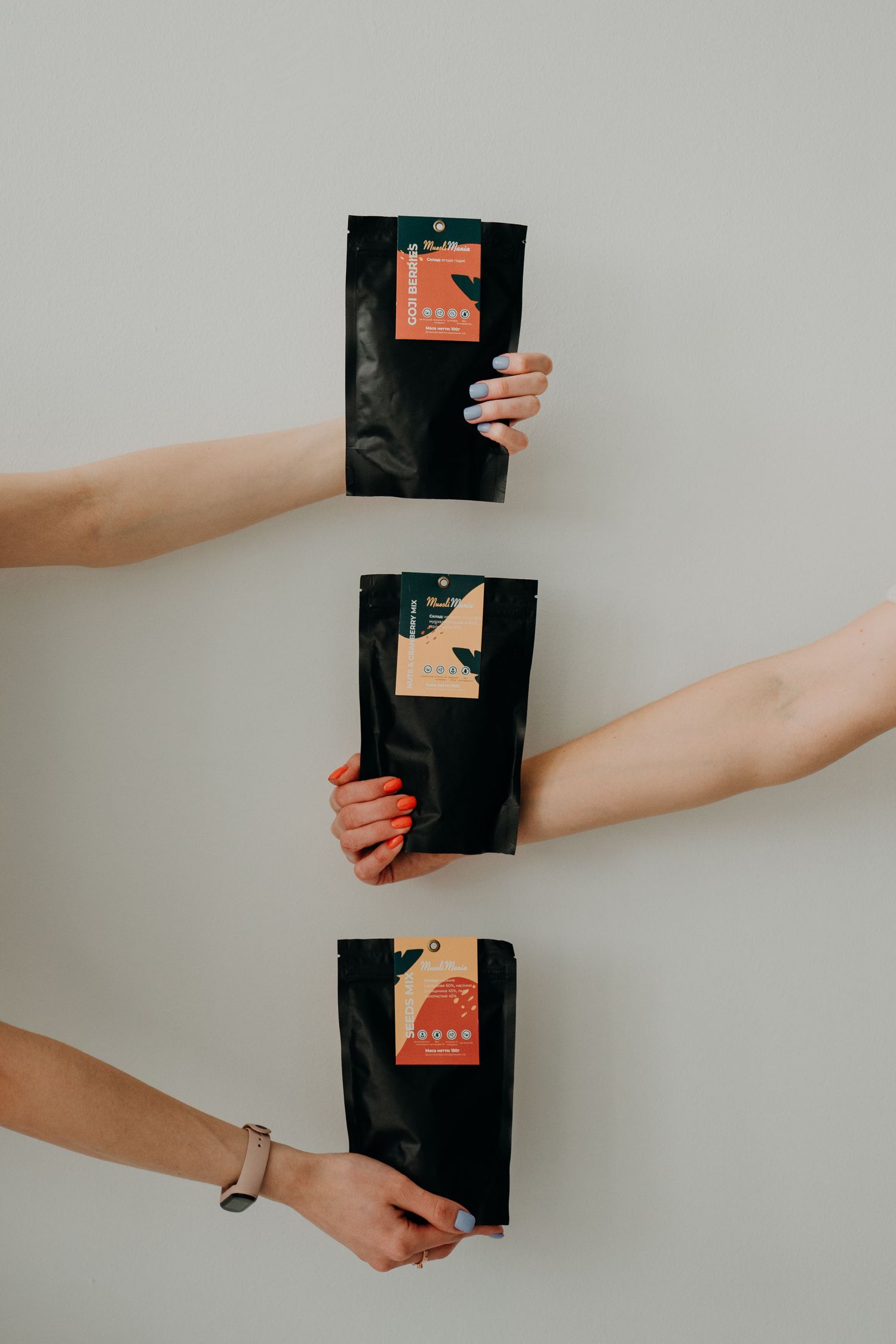 Three hands holding black coffee packaging bags with colorful labels against a light gray background.