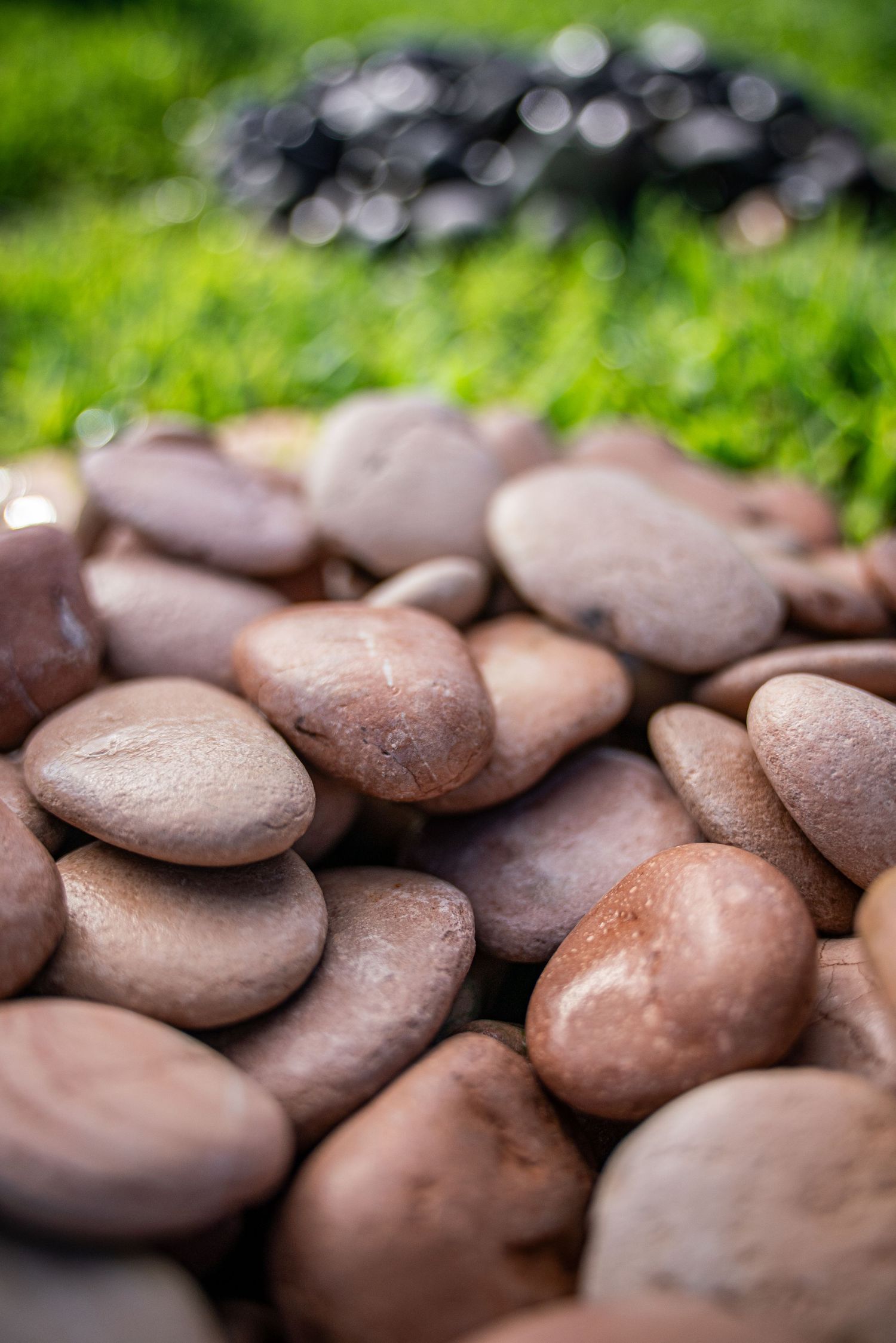 A pile of smooth brown river pebbles stacked together with green grass and dark rocks blurred in the background.
