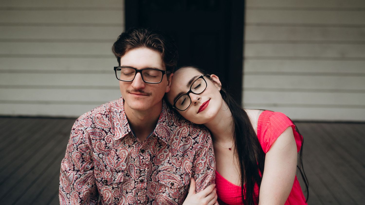 A couple sits together on a rustic white porch with matching outfits.