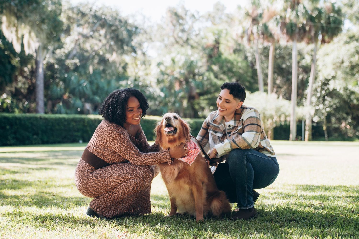 People and their golden retriever spending quality time together on grass under trees.