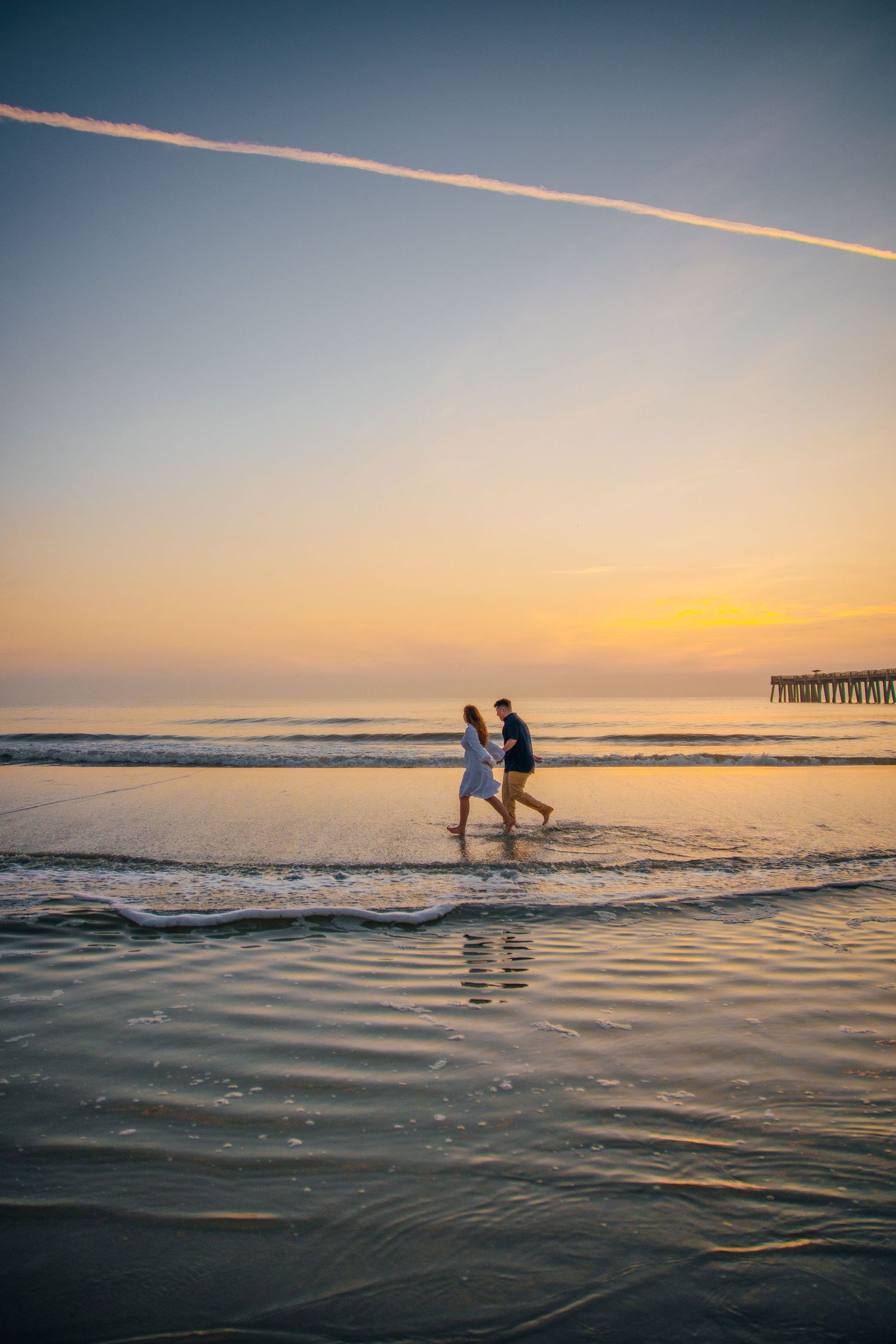 Silhouettes of two people wading in ocean water during a vibrant sunset.