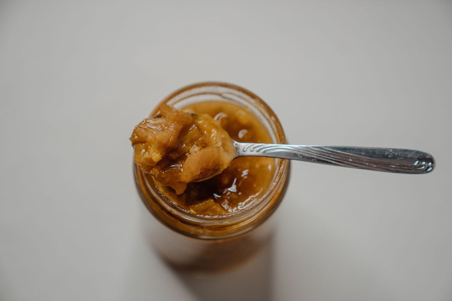 Close-up of a glass jar filled with caramel sauce and a silver spoon resting inside on a white surface.