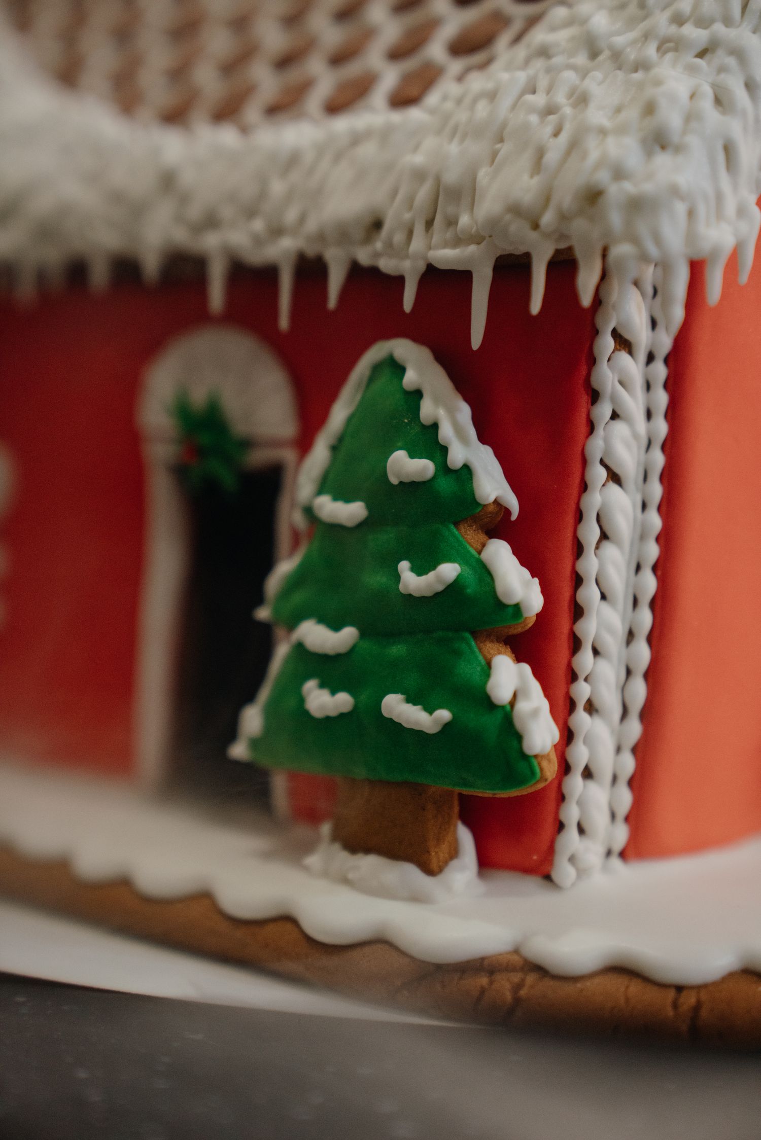 A decorative gingerbread house with white icing icicles and a green Christmas tree cookie covered in snow frosting.
