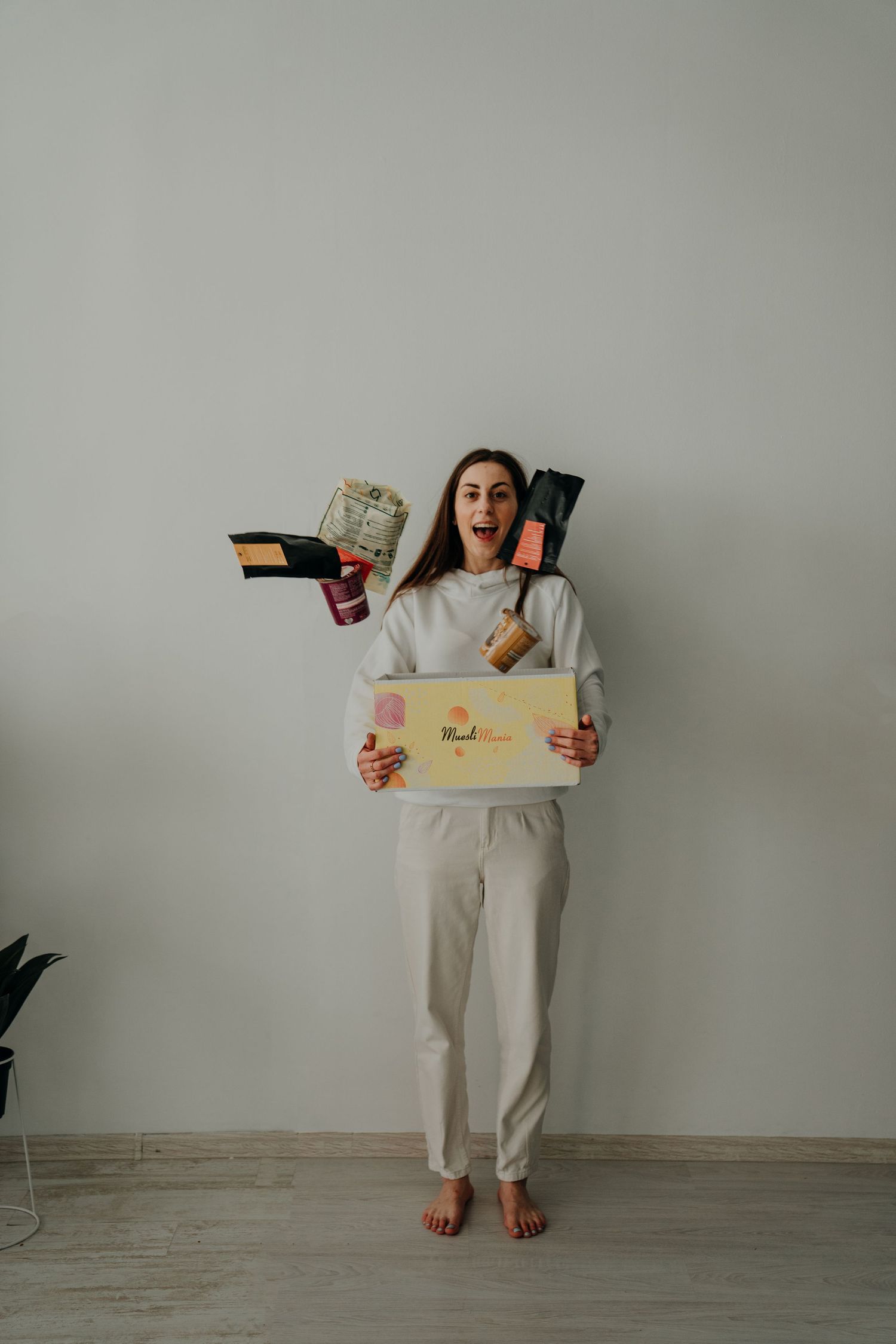 Excited woman holding a gift box and beauty products against a light gray wall, wearing a white casual outfit.
