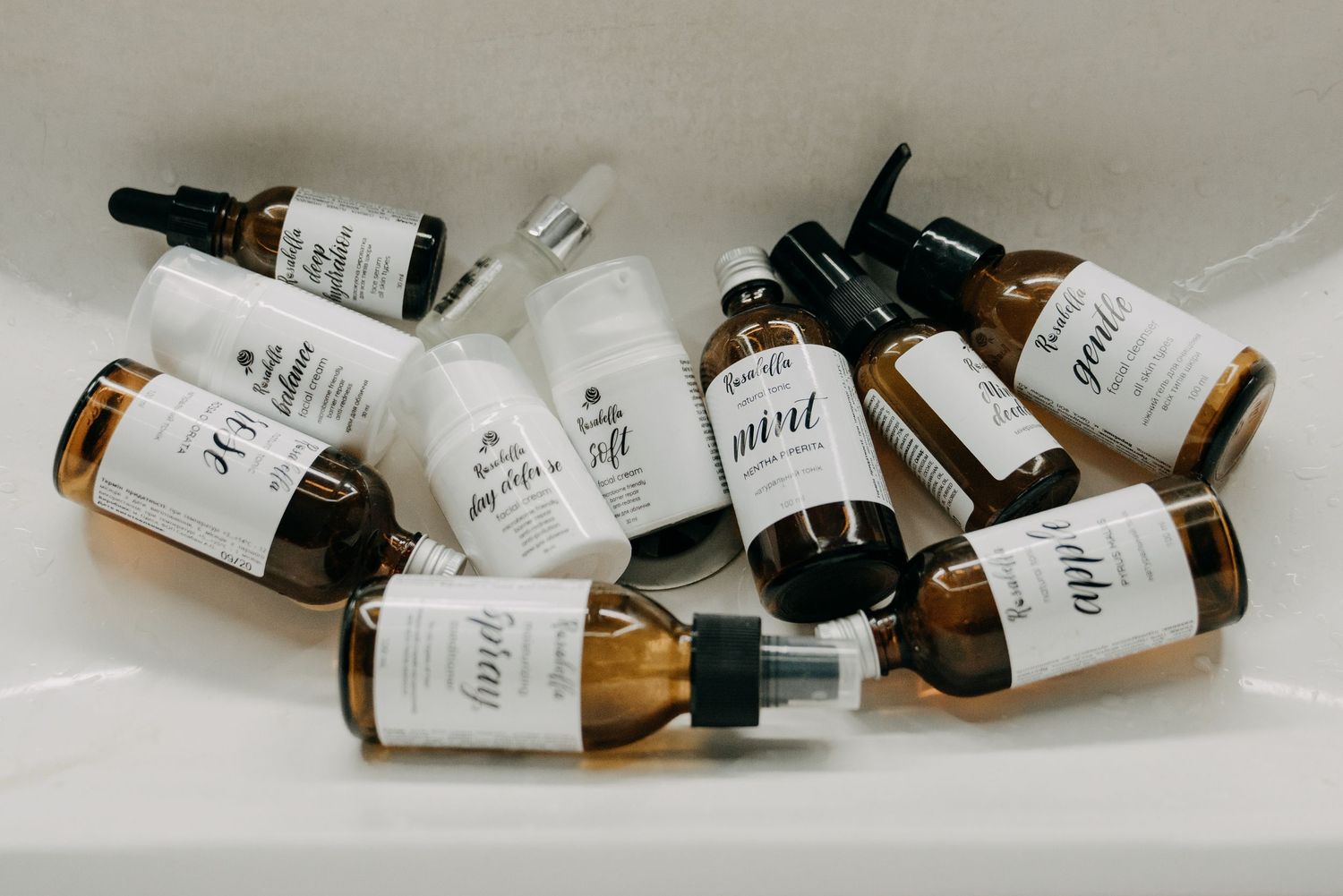 Amber glass dropper bottles of organic skincare serums and oils arranged in a white sink, showcasing a natural beauty product collection.