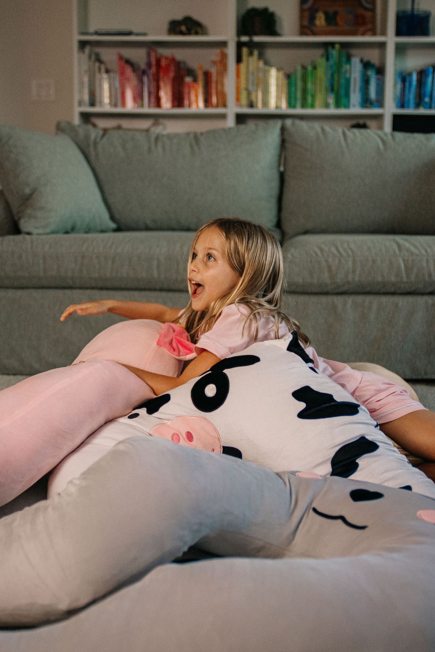 Young girl sitting on a cow-print bean bag chair in a living room, looking excited while watching TV.