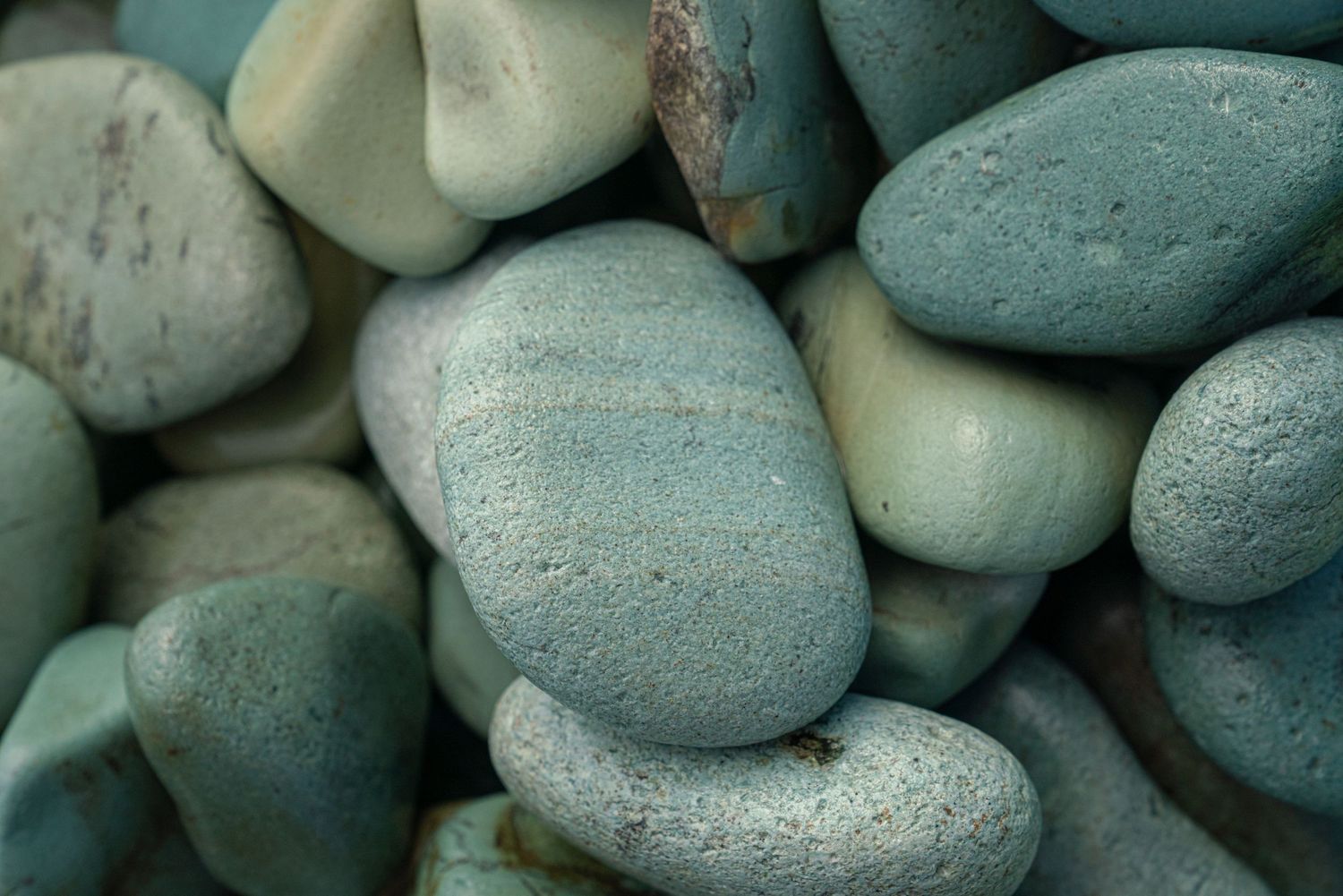 Close-up of smooth teal and green rounded pebbles stacked together.