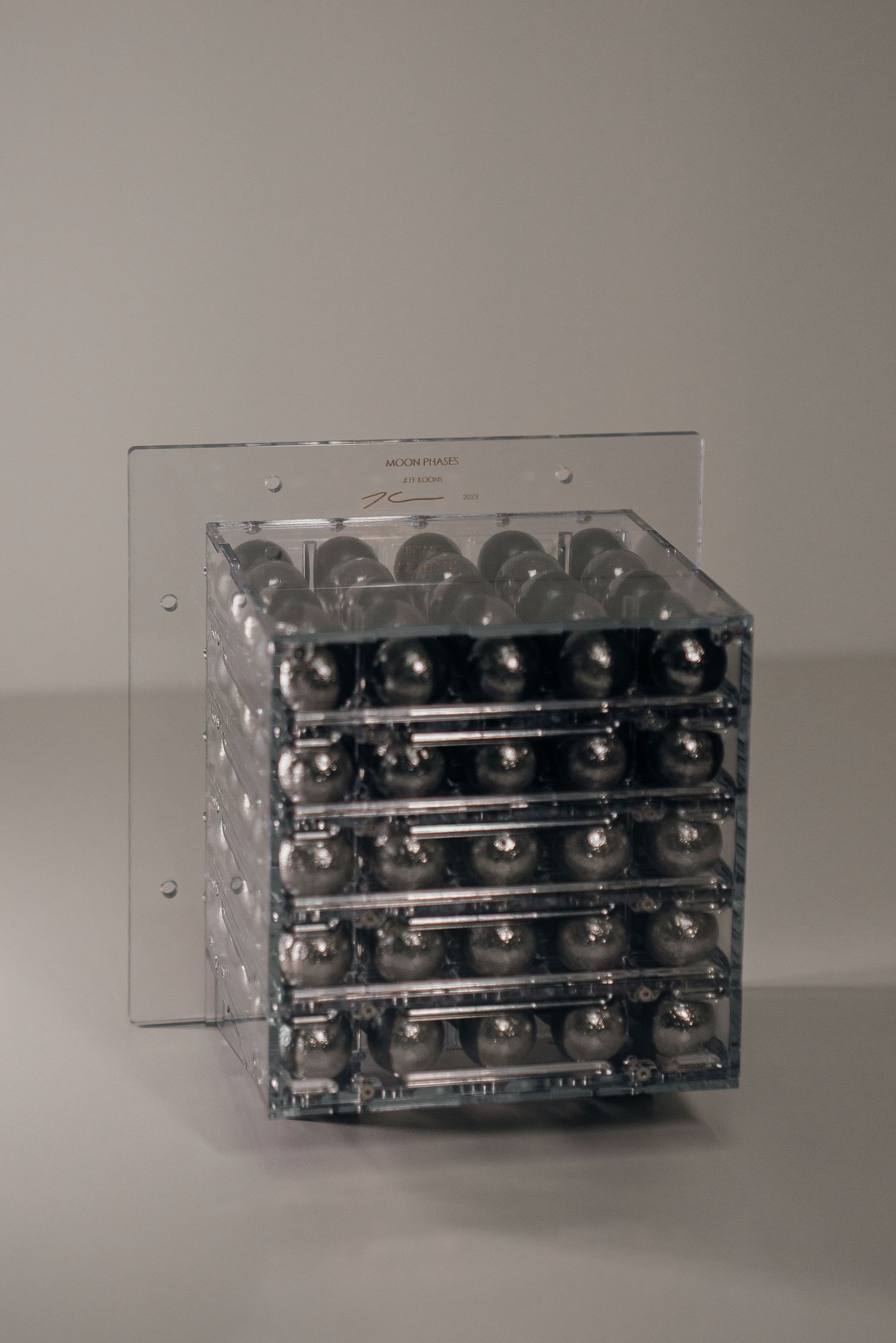 Clear acrylic cube display case filled with rows of shiny metallic steel balls arranged in a 5x5 grid pattern.