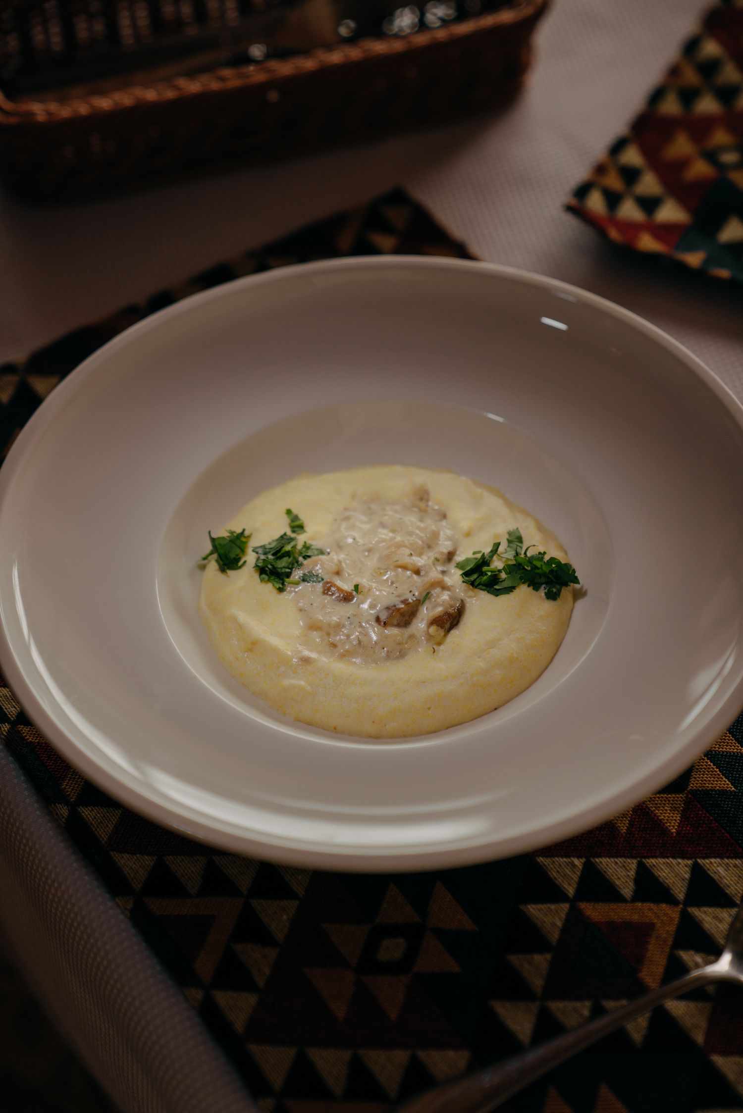 Creamy polenta topped with mushroom sauce and fresh parsley garnish served in a white bowl.