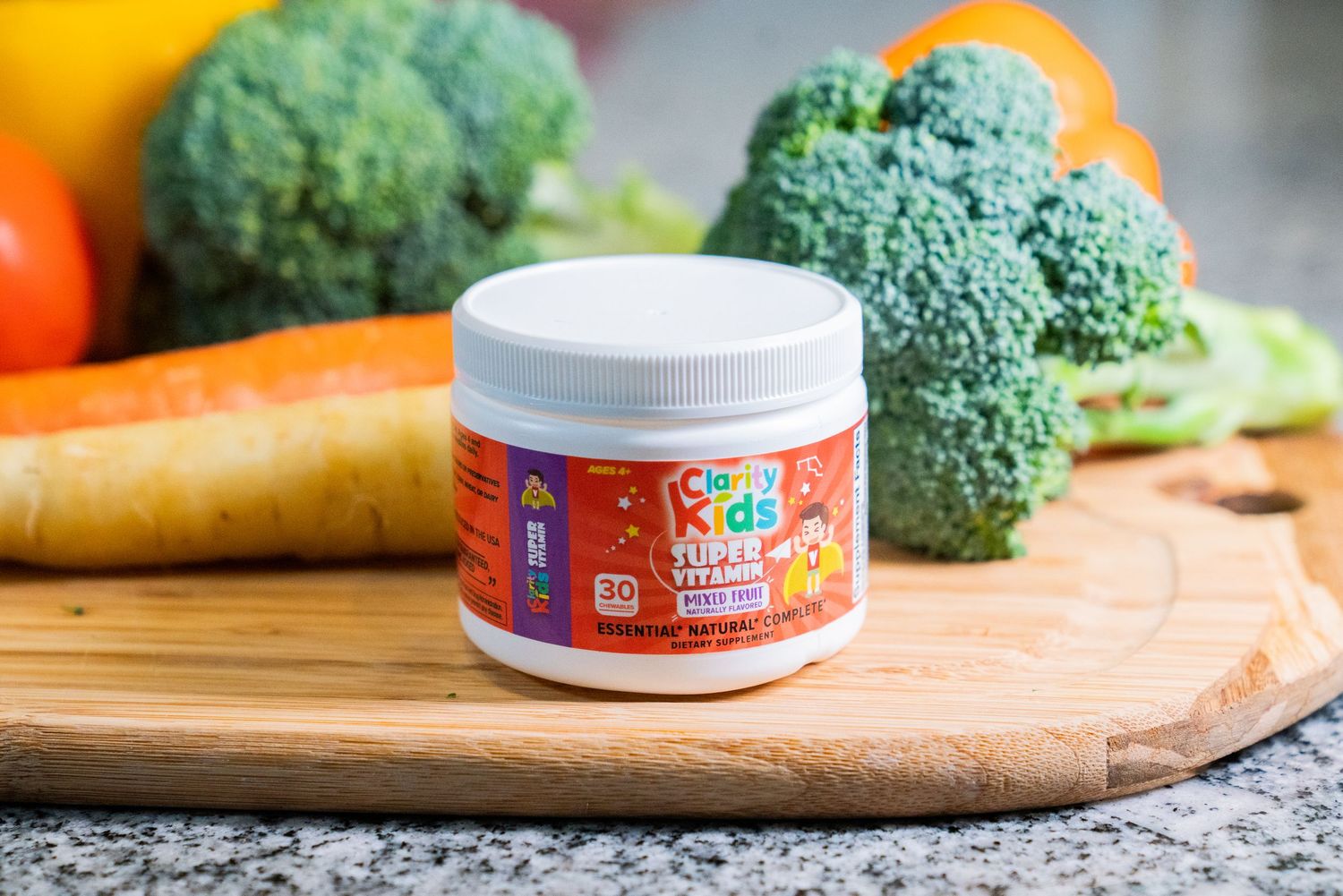 CrazyKidz Super Vitamins supplement jar on wooden cutting board surrounded by fresh broccoli, carrots, and vegetables.