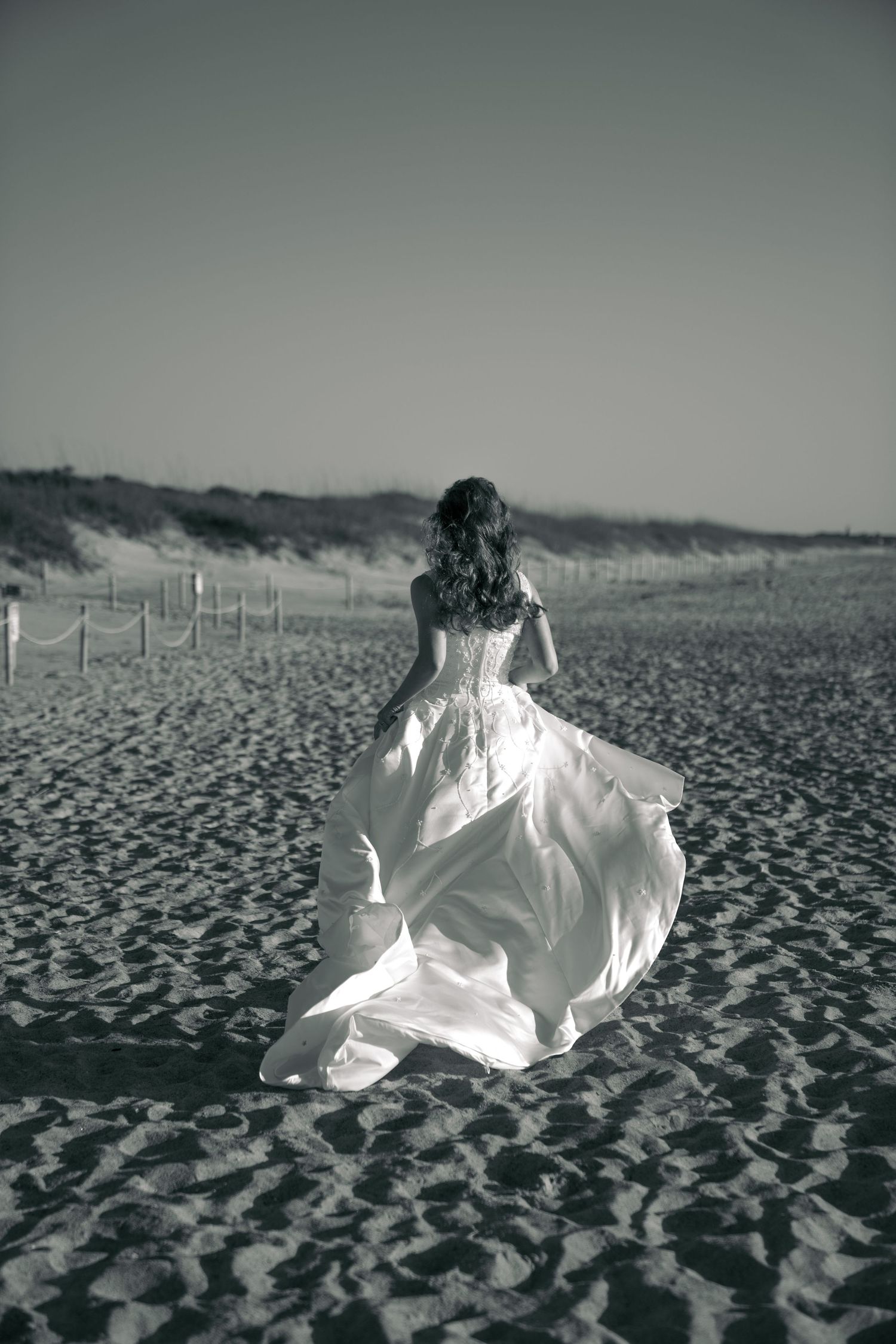 A flowing white dress twirls on a sandy beach in dramatic black and white photography.