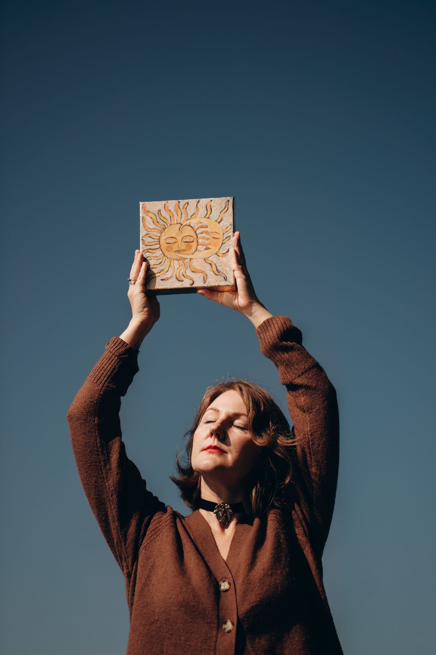 A series of artistic portraits showing someone in a brown sweater holding a wooden object against a blue backdrop.