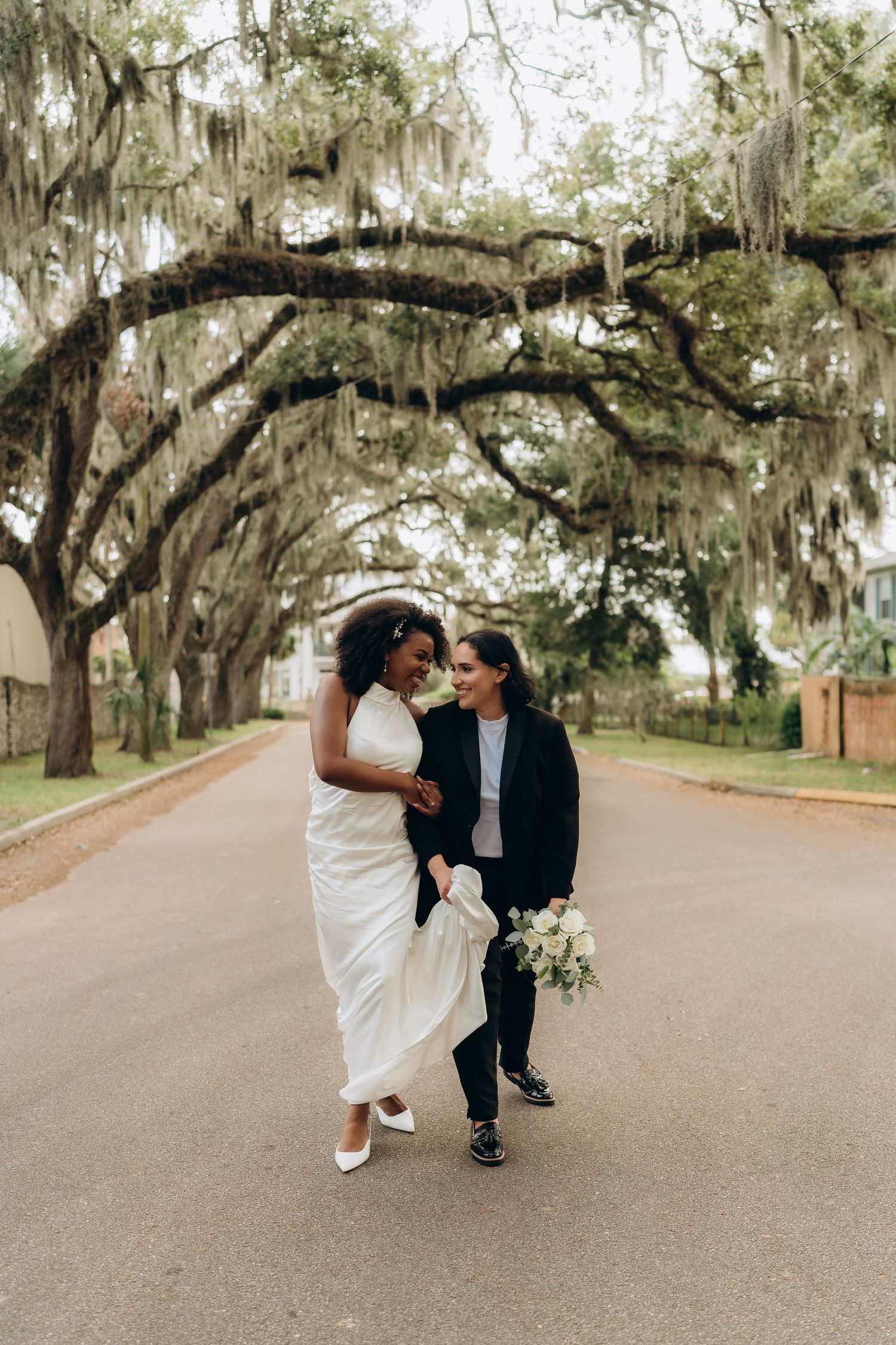 A playful wedding photoshoot under moss-draped oak trees on a scenic road.