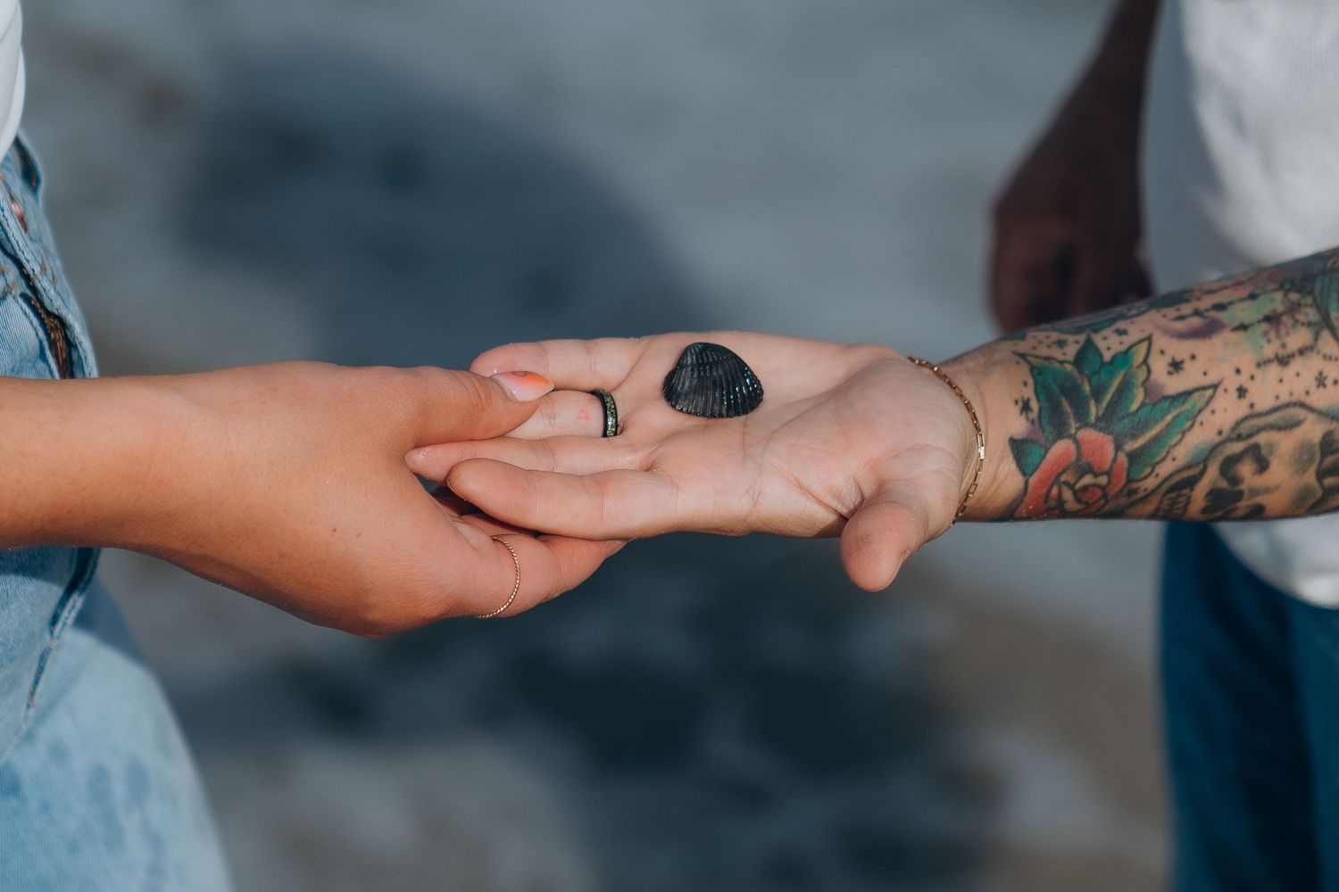 Close-up of tattooed and non-tattooed hands reaching towards each other against a blue background.