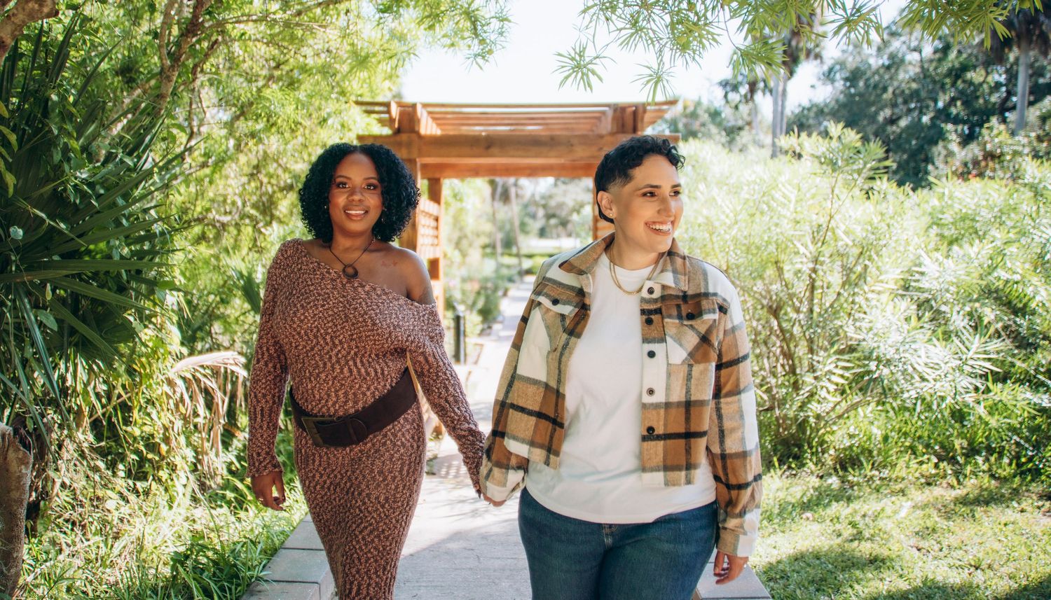 Two people hold hands while walking along a garden path on a bright sunny day.