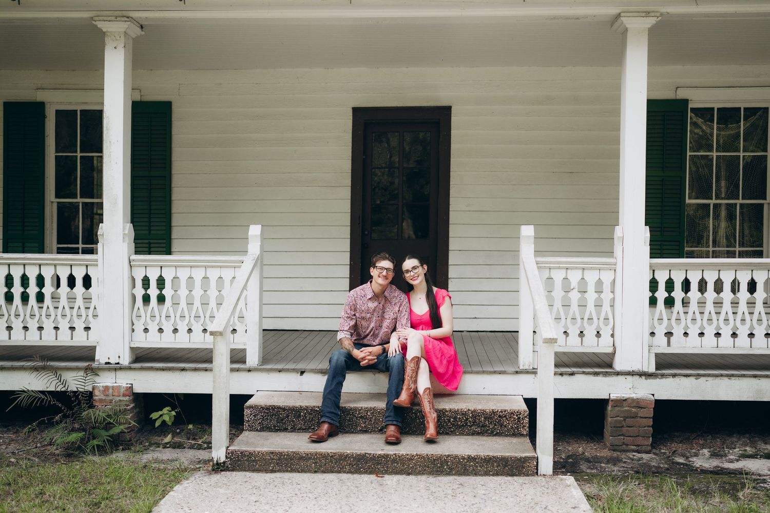 A white farmhouse porch with classic columns and railing extends across the front of the building.