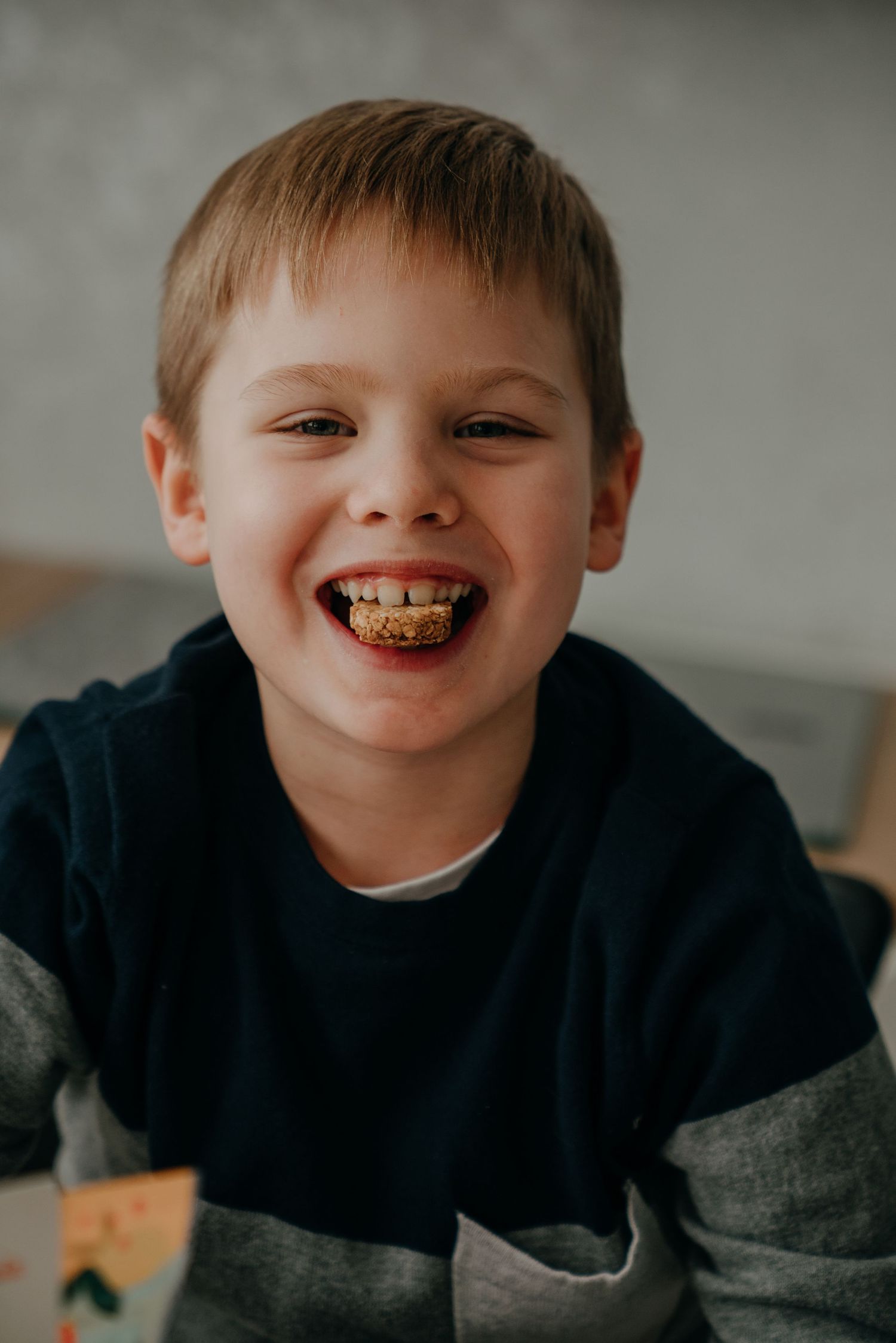 Happy young boy laughing with food in his teeth, wearing a navy blue sweater, portrait photo.