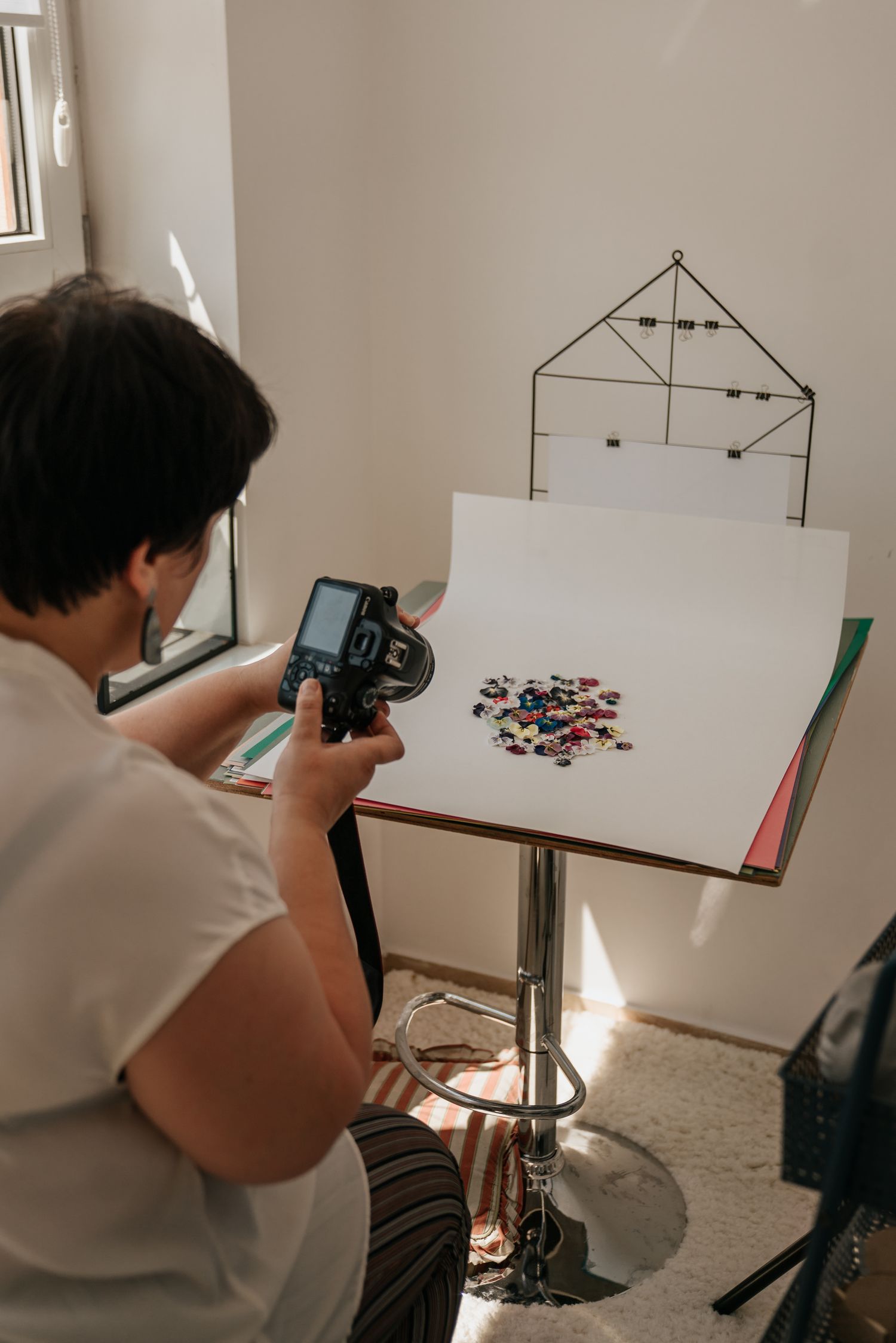 Photographer capturing colorful buttons on a white backdrop in a small home studio setup with natural light.