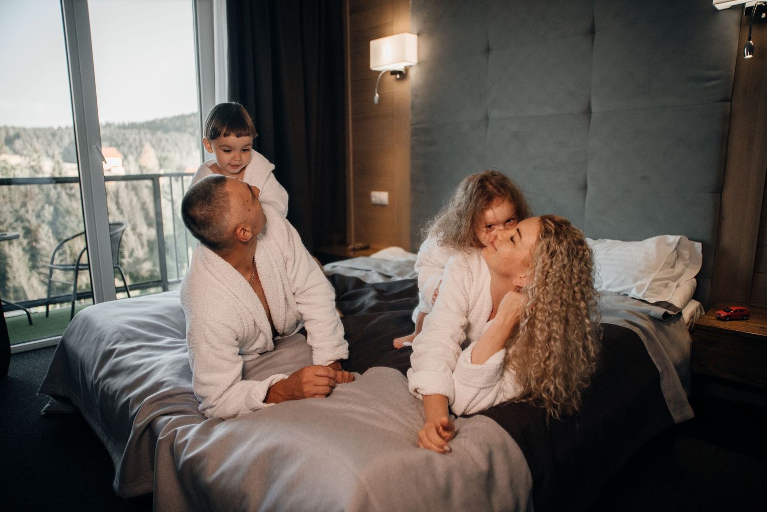 Family in white robes enjoying a cozy moment together on a bed in a modern hotel room.