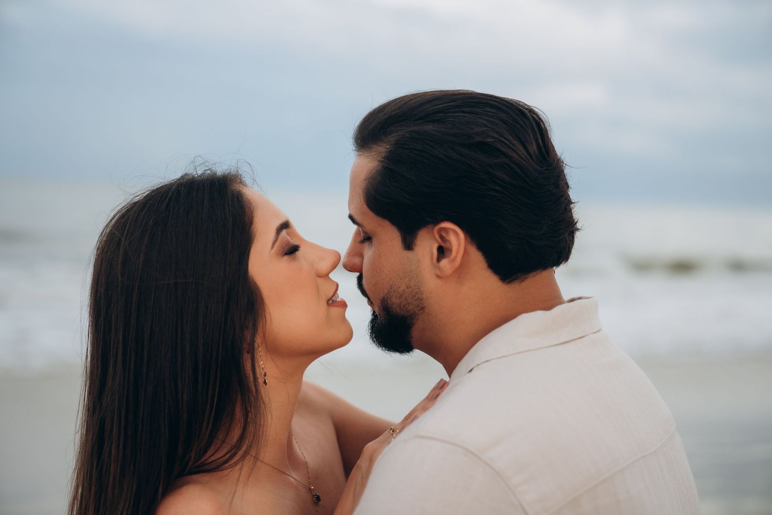 Intimate beach portrait of a couple in white clothing sharing a romantic moment.