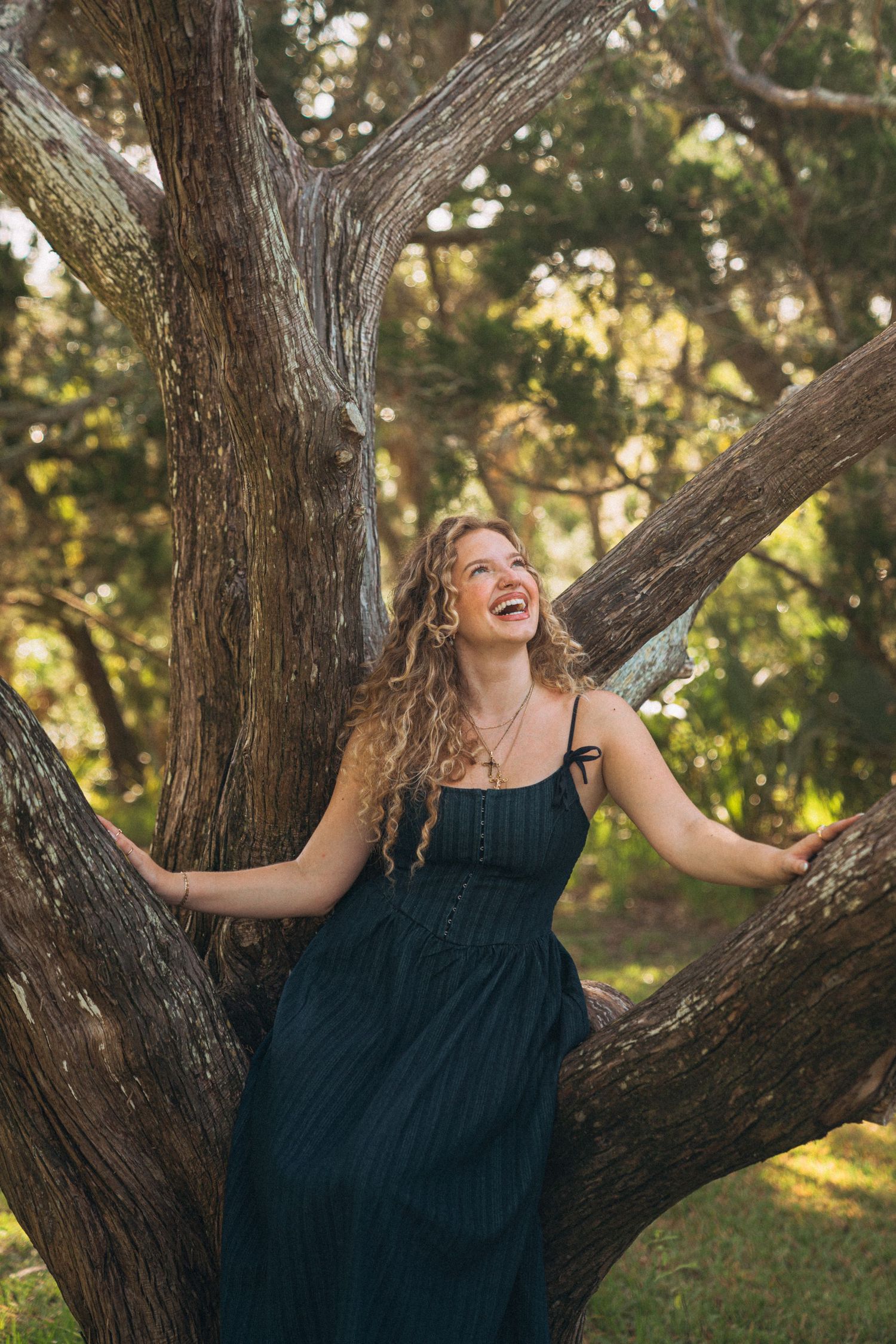 Playful pose against a large tree trunk in dappled sunlight.