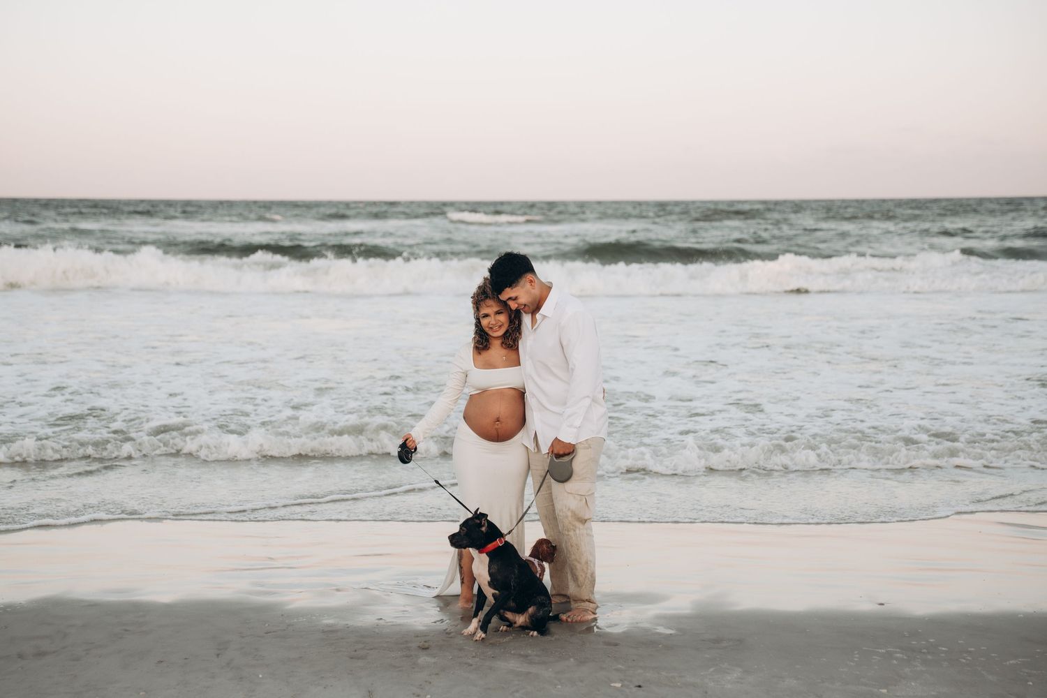 A couple shares intimate moments on a windy beach with waves crashing behind them.