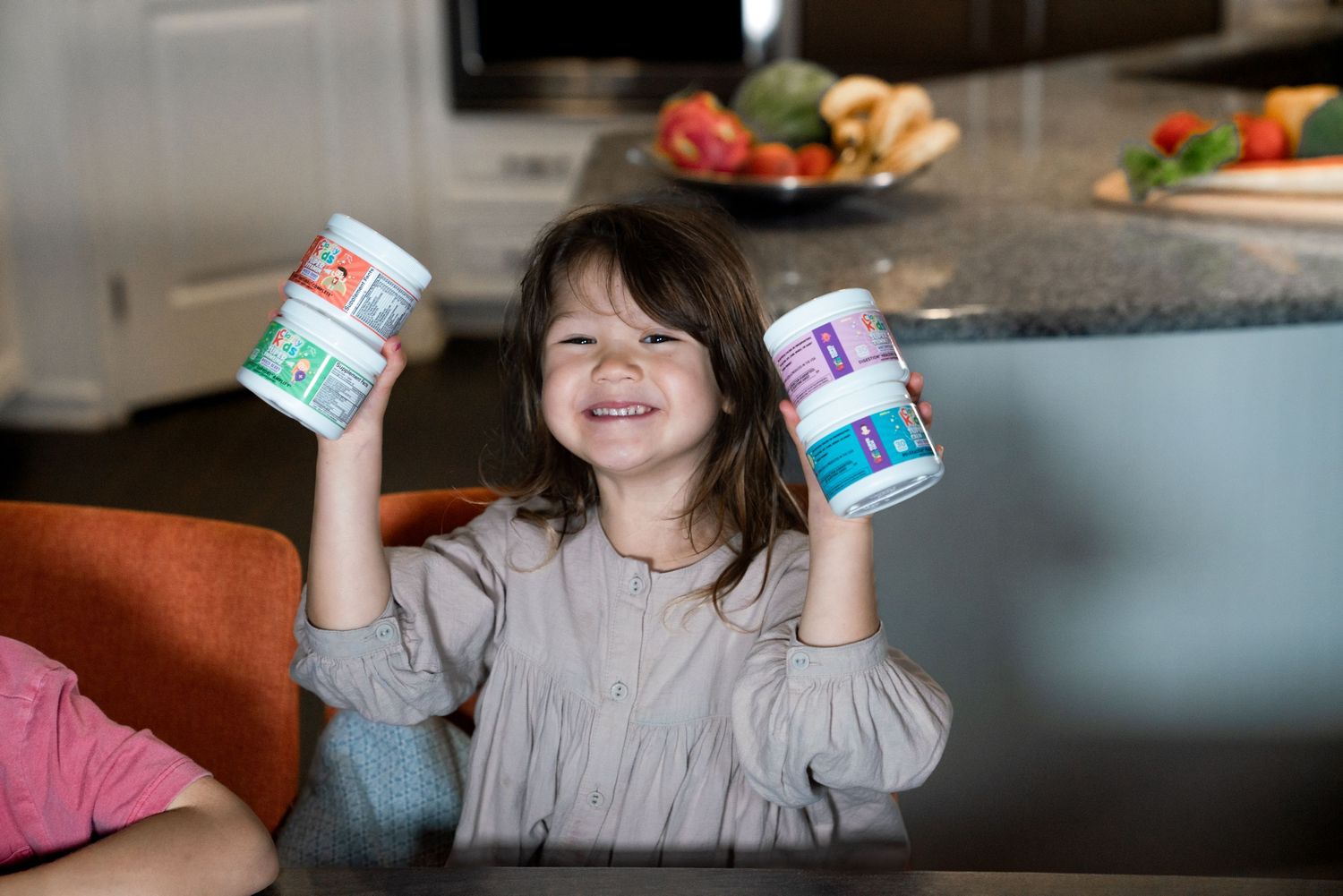 Happy young girl smiling and holding up two colorful canisters in a bright modern kitchen.