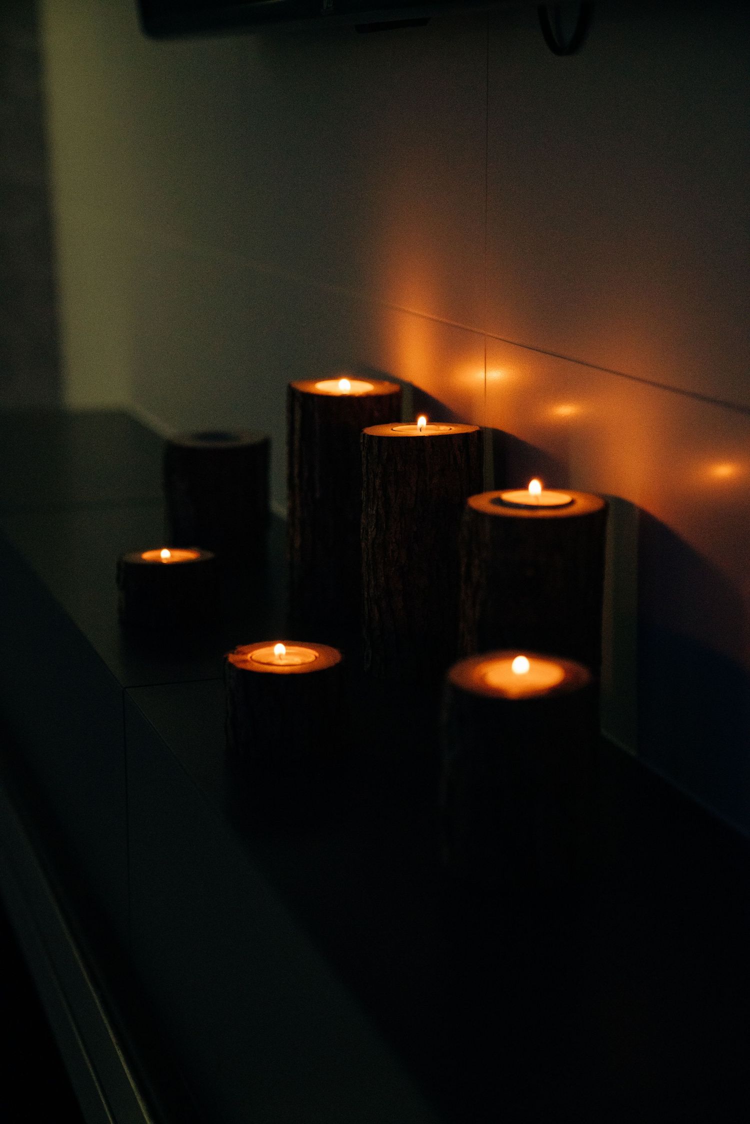 Rustic wooden log candle holders with glowing tea light candles arranged on a dark shelf creating warm ambient light.