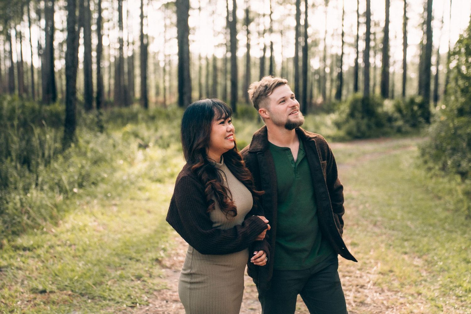 Couple enjoying a tender moment while sitting on fallen leaves in a sunlit autumn forest.