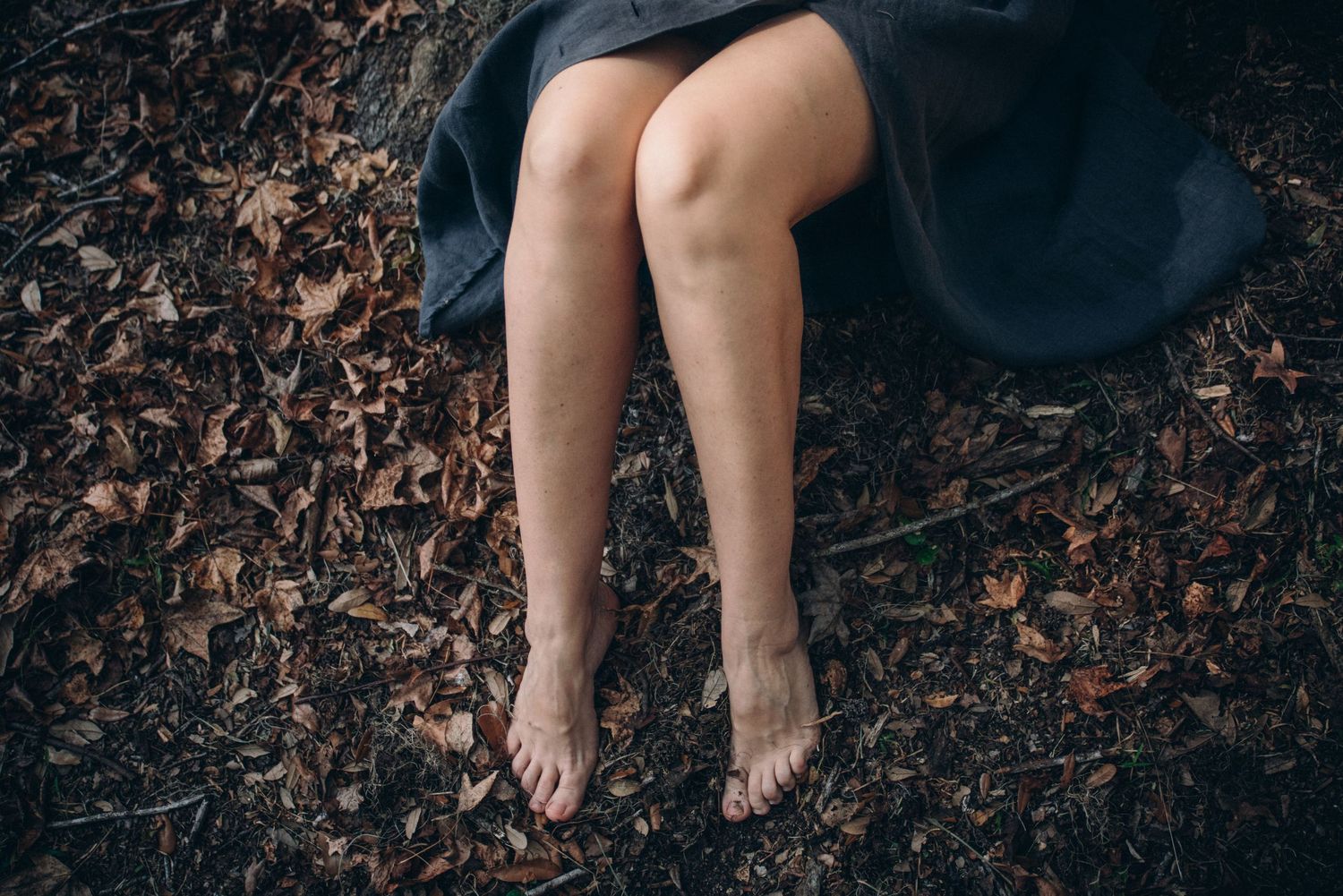 Bare feet walking on dark autumn leaves scattered across the ground.