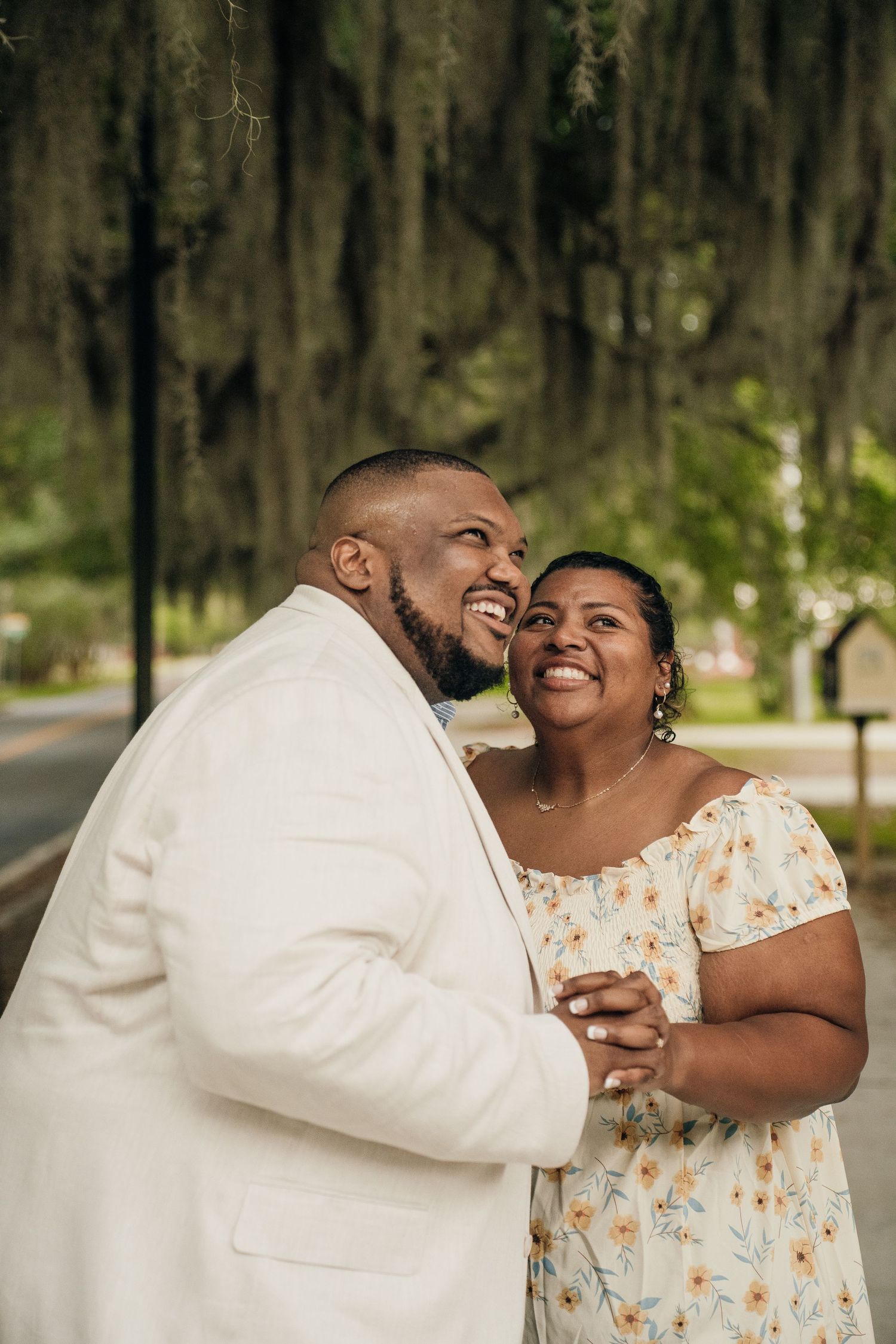 A couple shares laughter while embracing outdoors in coordinated cream and floral outfits.