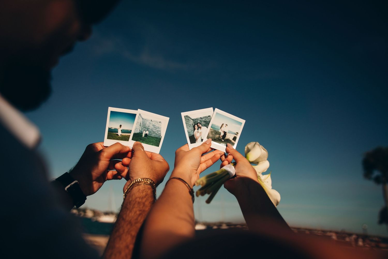 Two people holding Polaroid instant photos against a blue sky at golden hour outdoors.