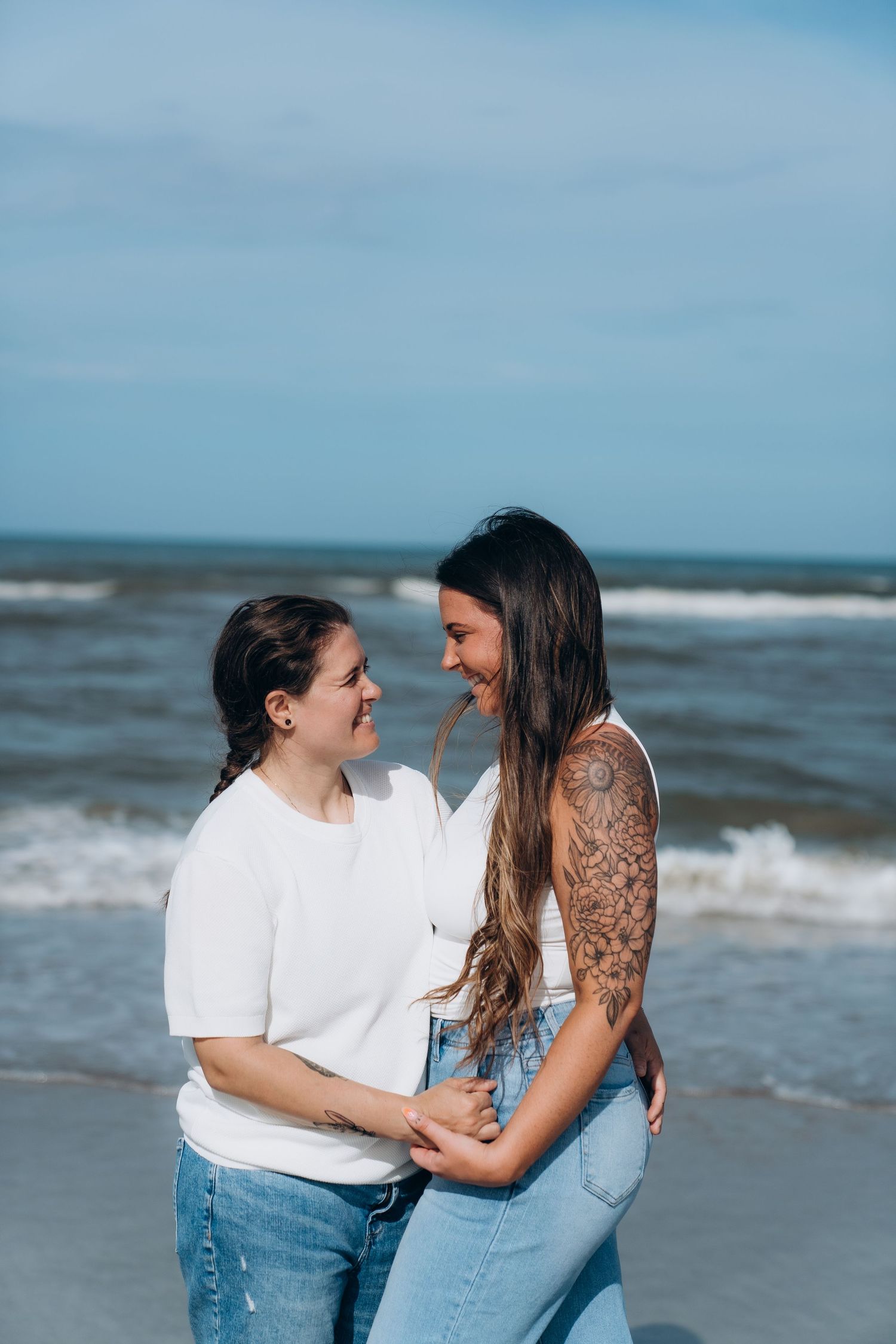 A couple in denim and white shirts sharing an intimate moment by the ocean.
