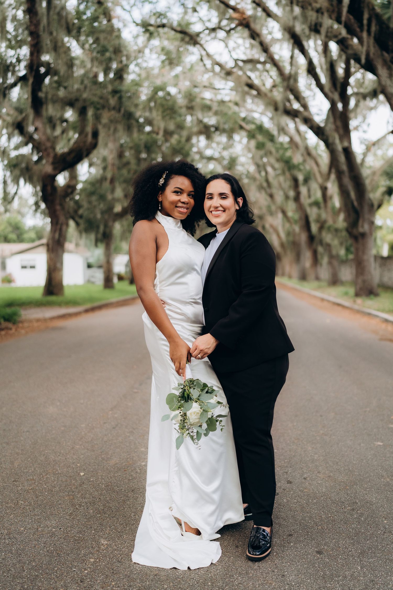 A couple shares a joyful moment on a road lined with Spanish moss-draped oak trees.