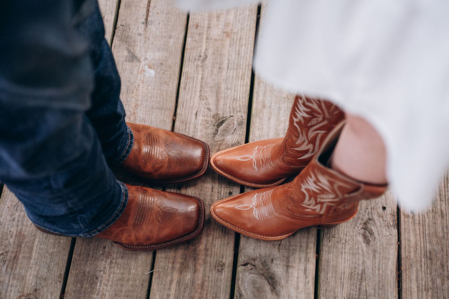 Two pairs of matching brown leather cowboy boots positioned side by side on a wooden deck.