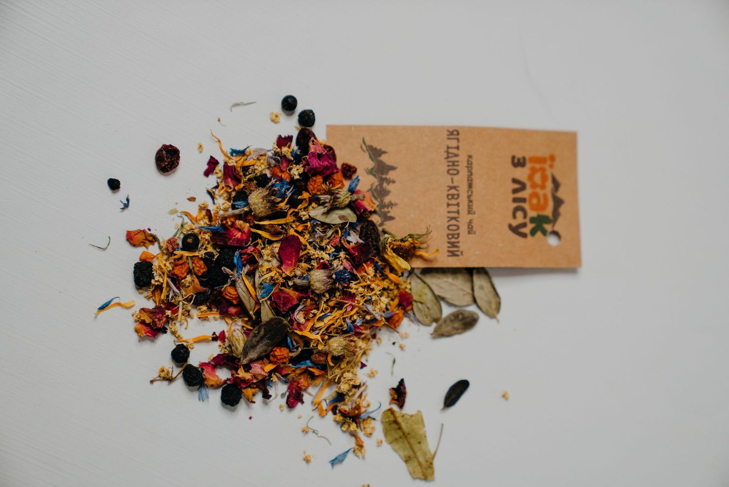 Colorful loose leaf herbal tea blend with dried flowers and berries spilling from a kraft paper packet.