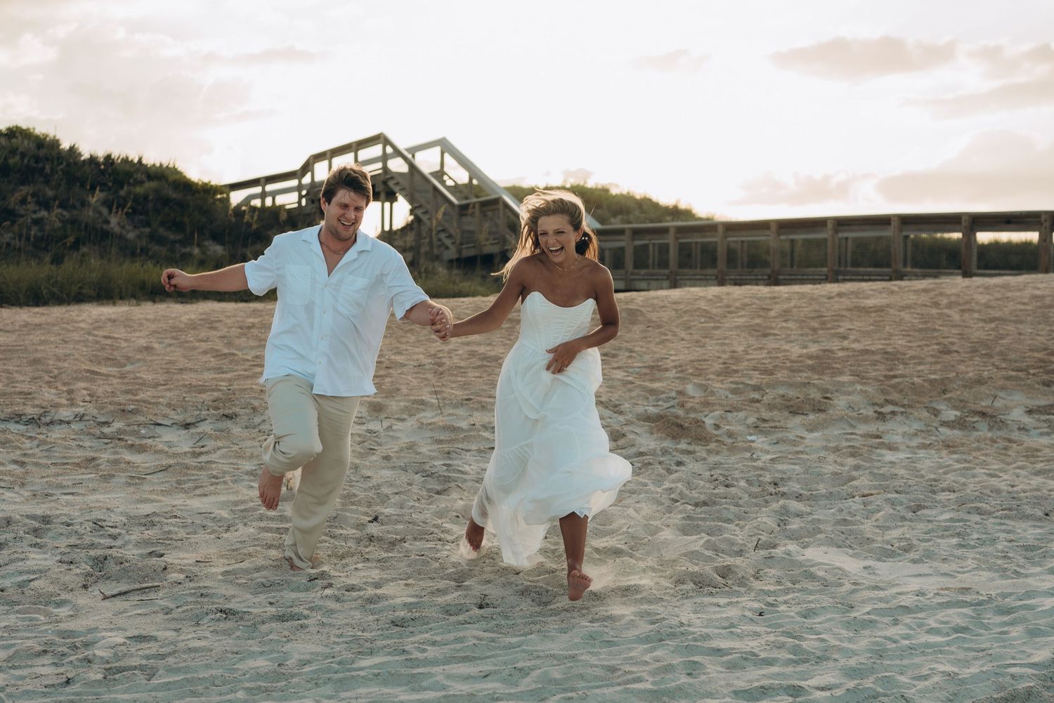 Playful couple running and splashing in the sand at the beach during golden hour.