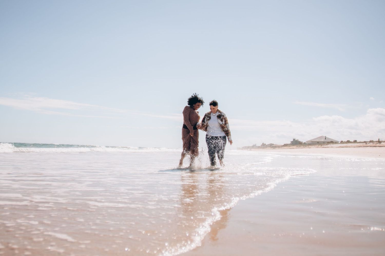People walking along a serene beach shoreline with gentle waves and soft sand on a sunny day.